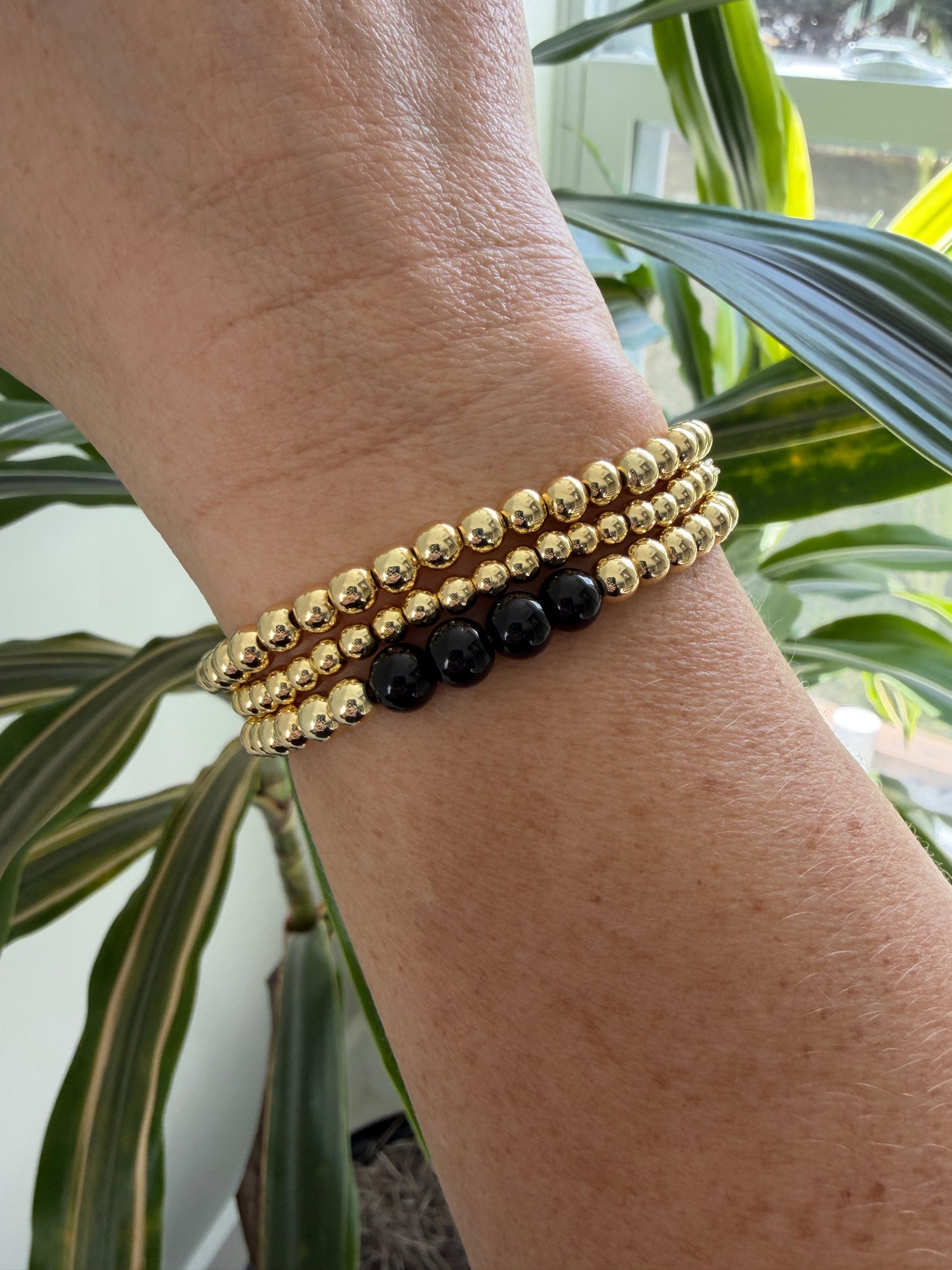 Close-up of a wrist wearing two beaded bracelets with a plant in the background