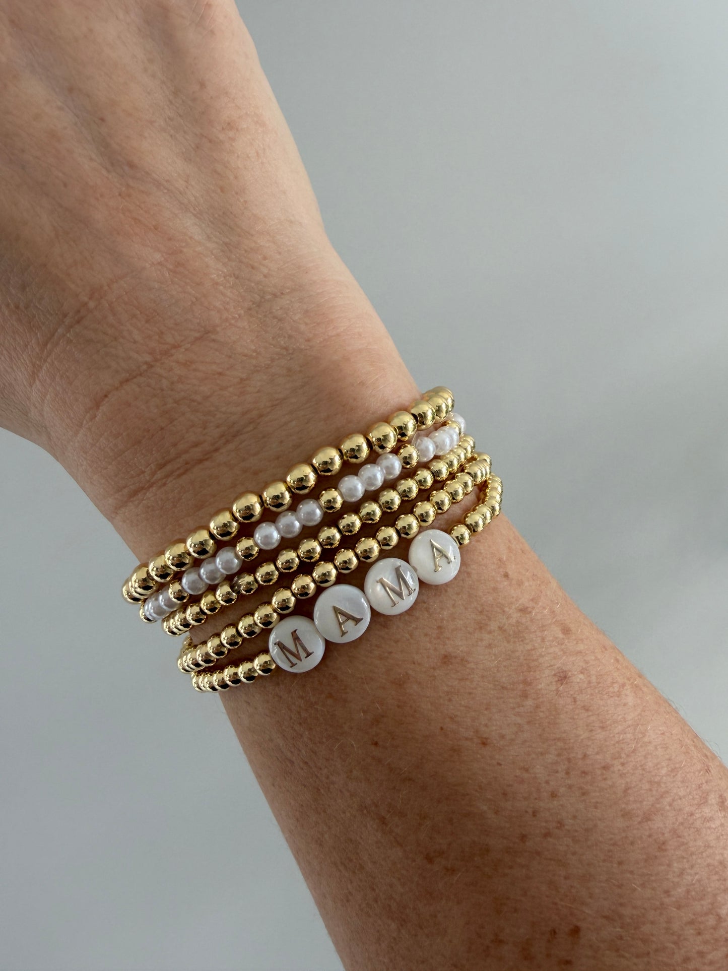 Wrist wearing multiple gold and pearl beaded bracelets on a neutral background