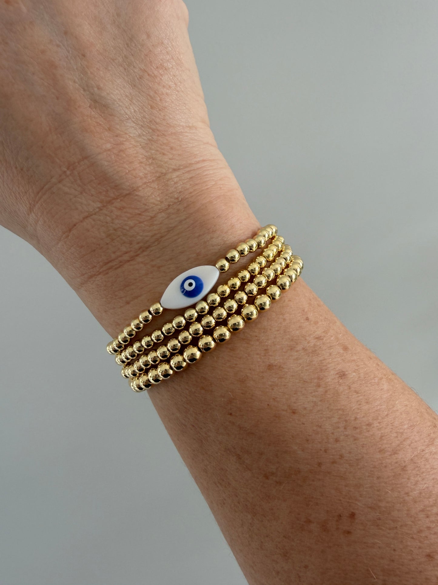 Gold-filled evil eye bracelet stacked with minimalist gold bracelets