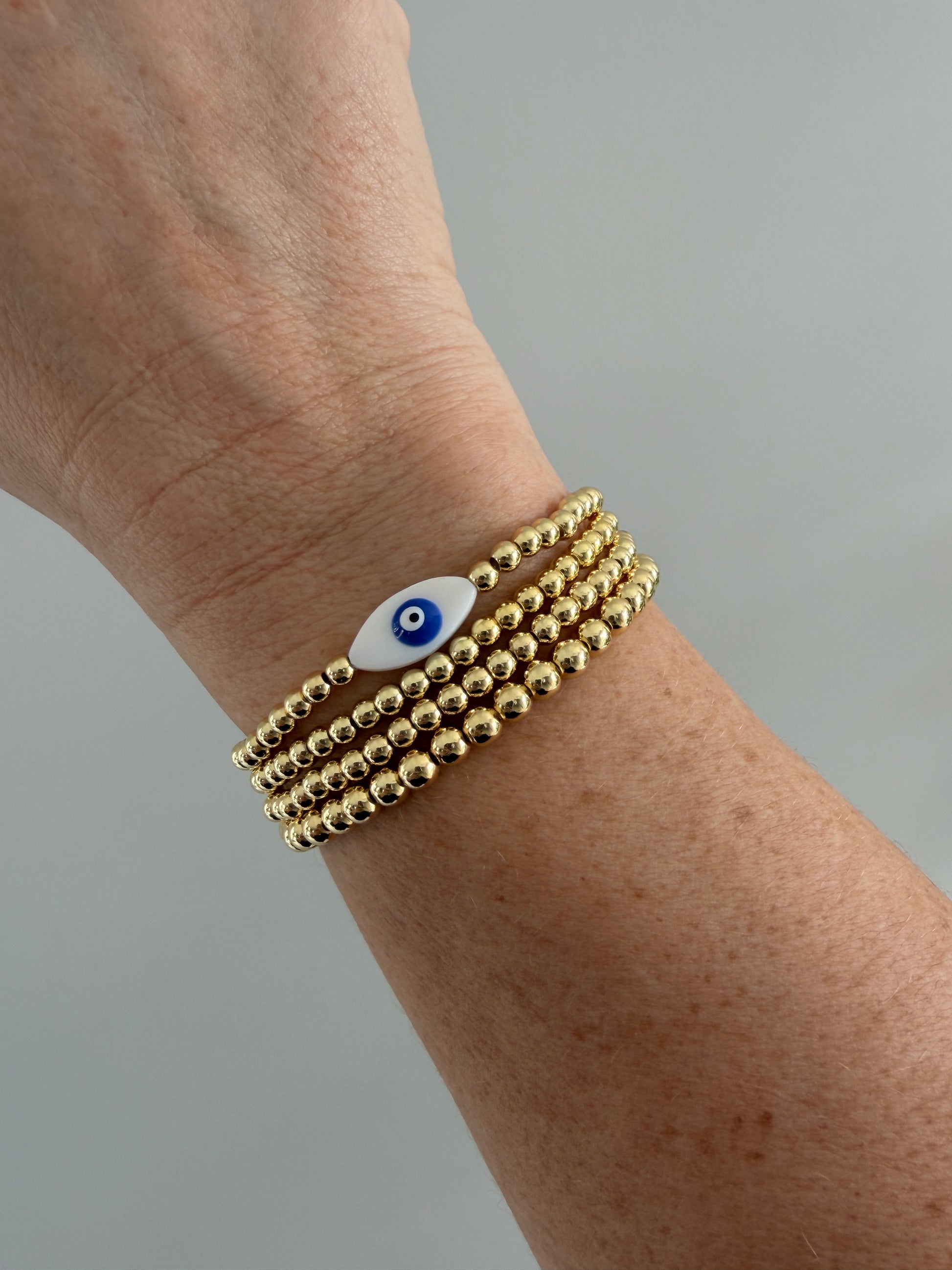 Gold-filled evil eye bracelet stacked with minimalist gold bracelets