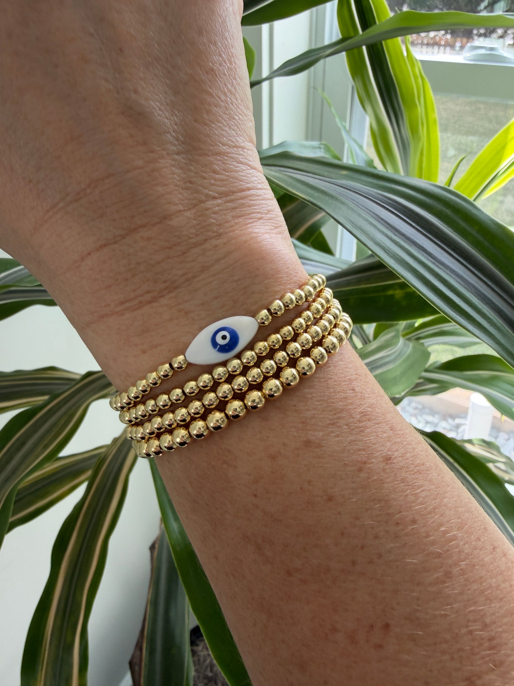Gold-filled evil eye bracelet stacked with minimalist gold bracelets