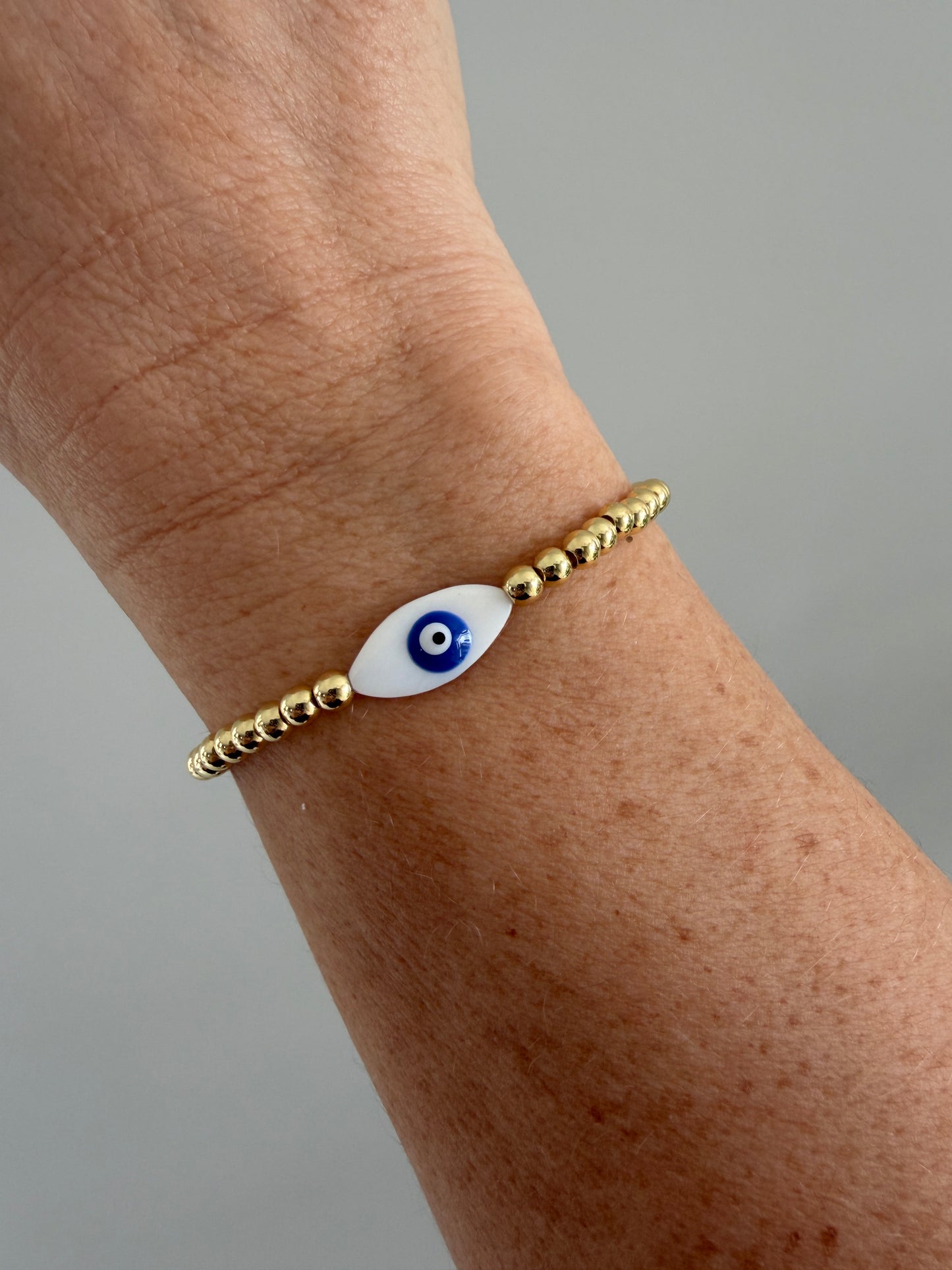 Gold bracelet with an eye charm on a wrist against a gray background