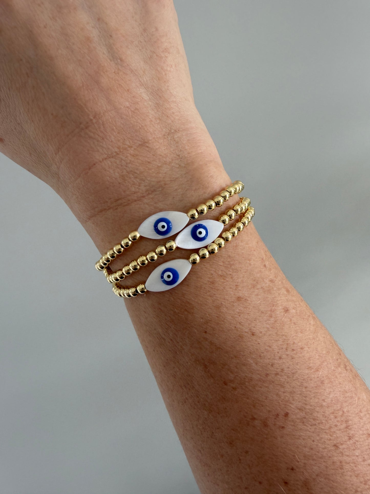 gold bracelets with eye-shaped charms on a wrist against a gray background