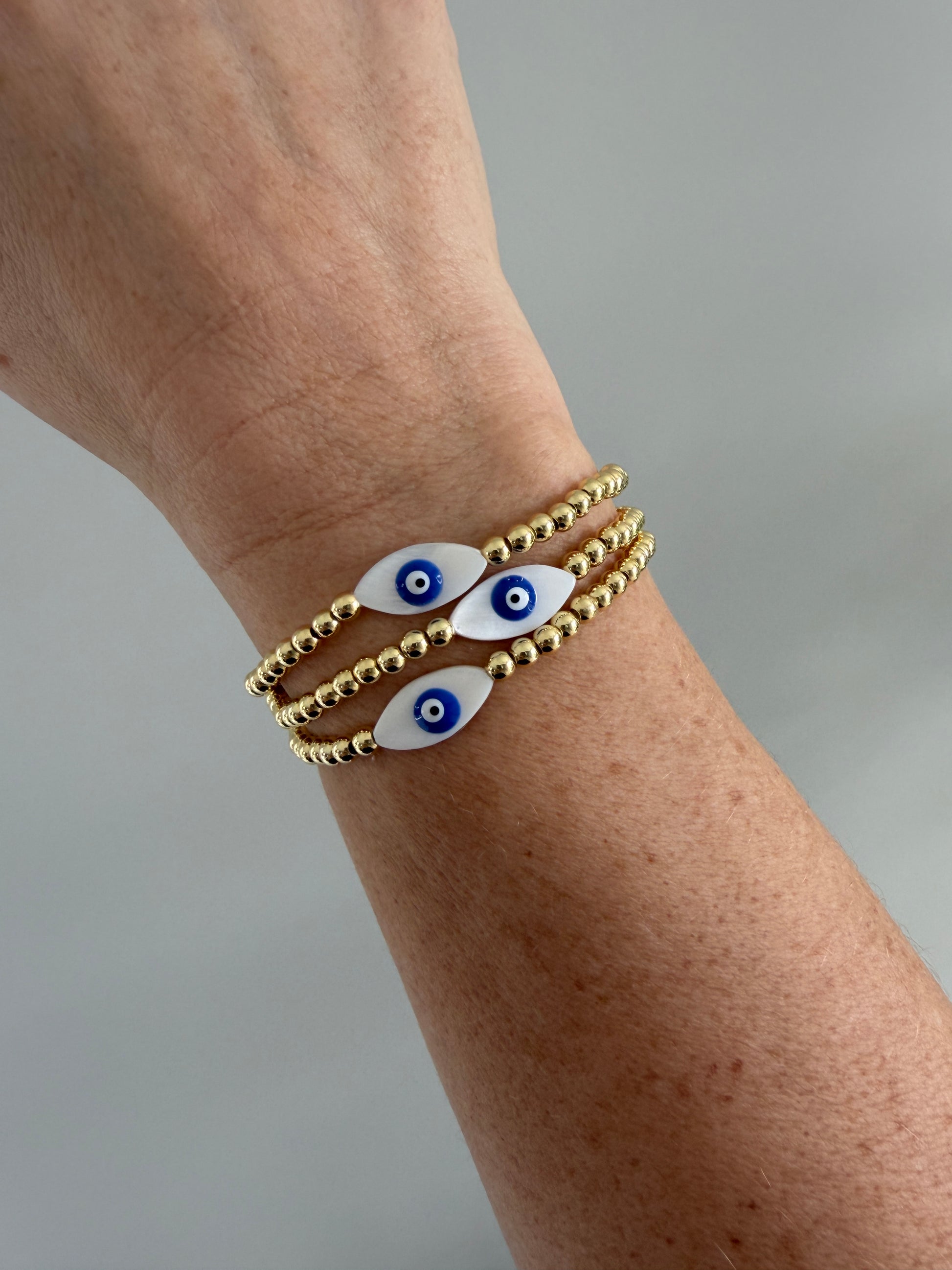 gold bracelets with eye-shaped charms on a wrist against a gray background