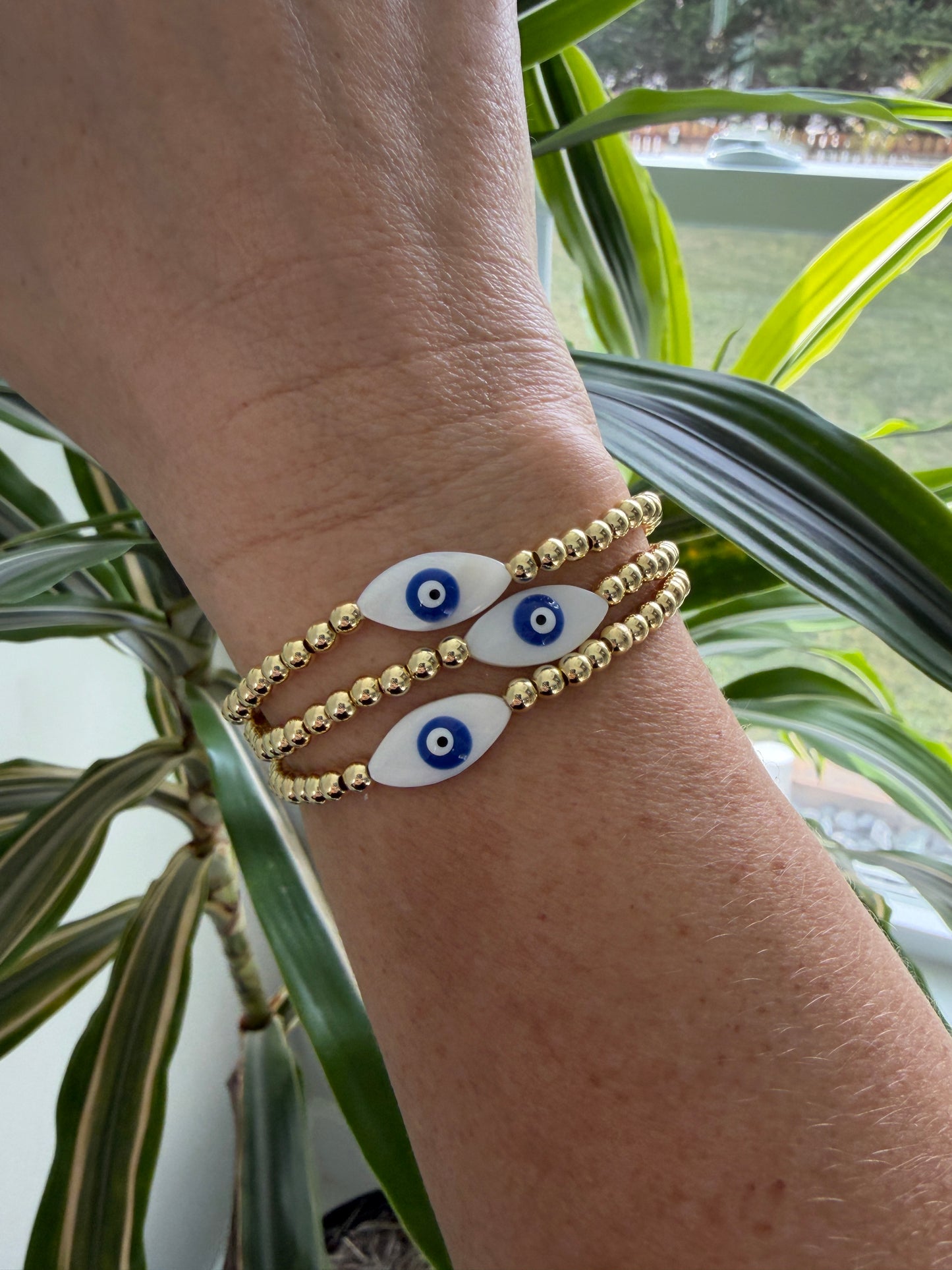 Bracelet with eye-shaped beads on a wrist, surrounded by green plants.