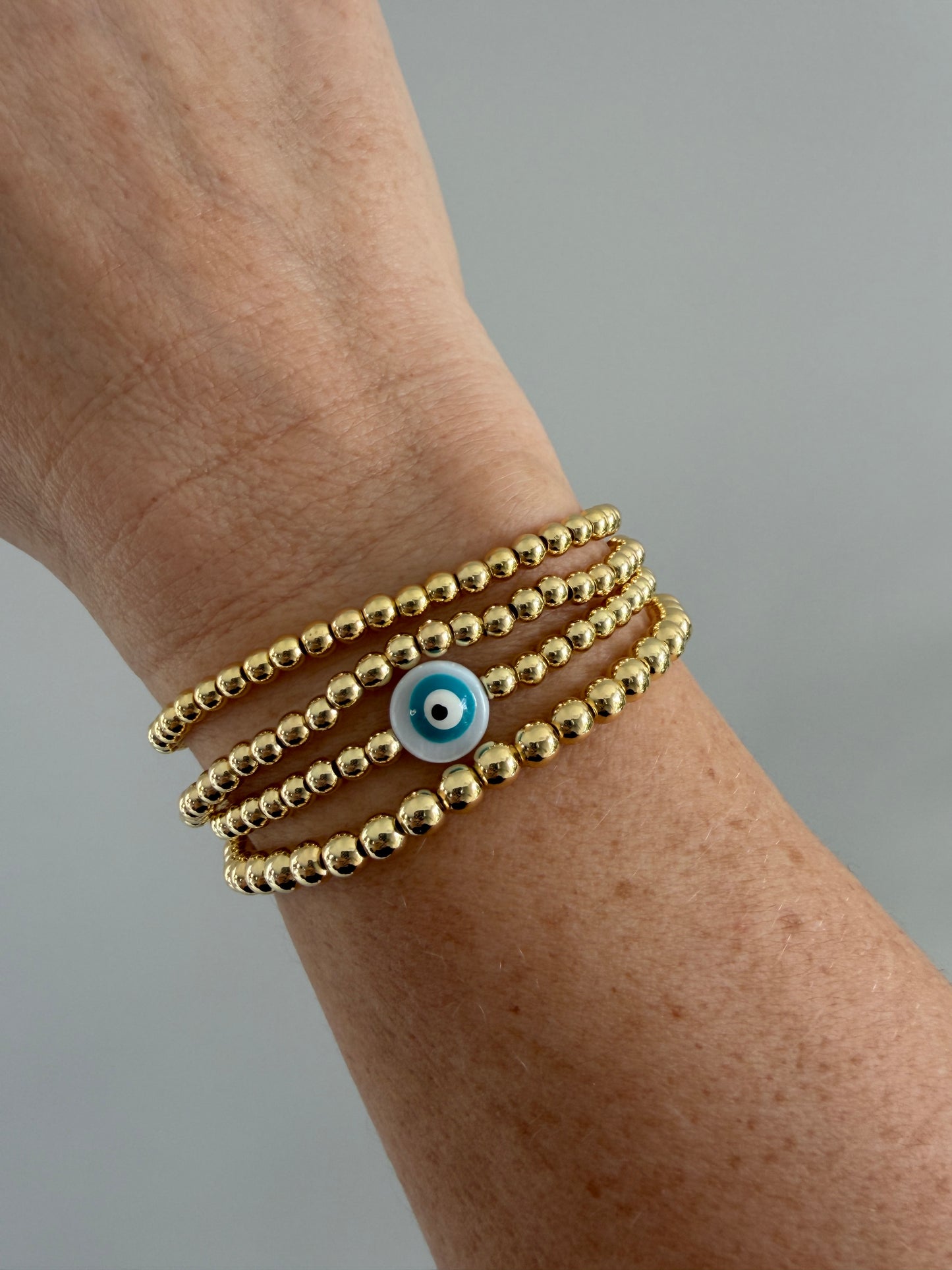 Gold-filled evil eye bracelet stacked with minimalist gold bracelets