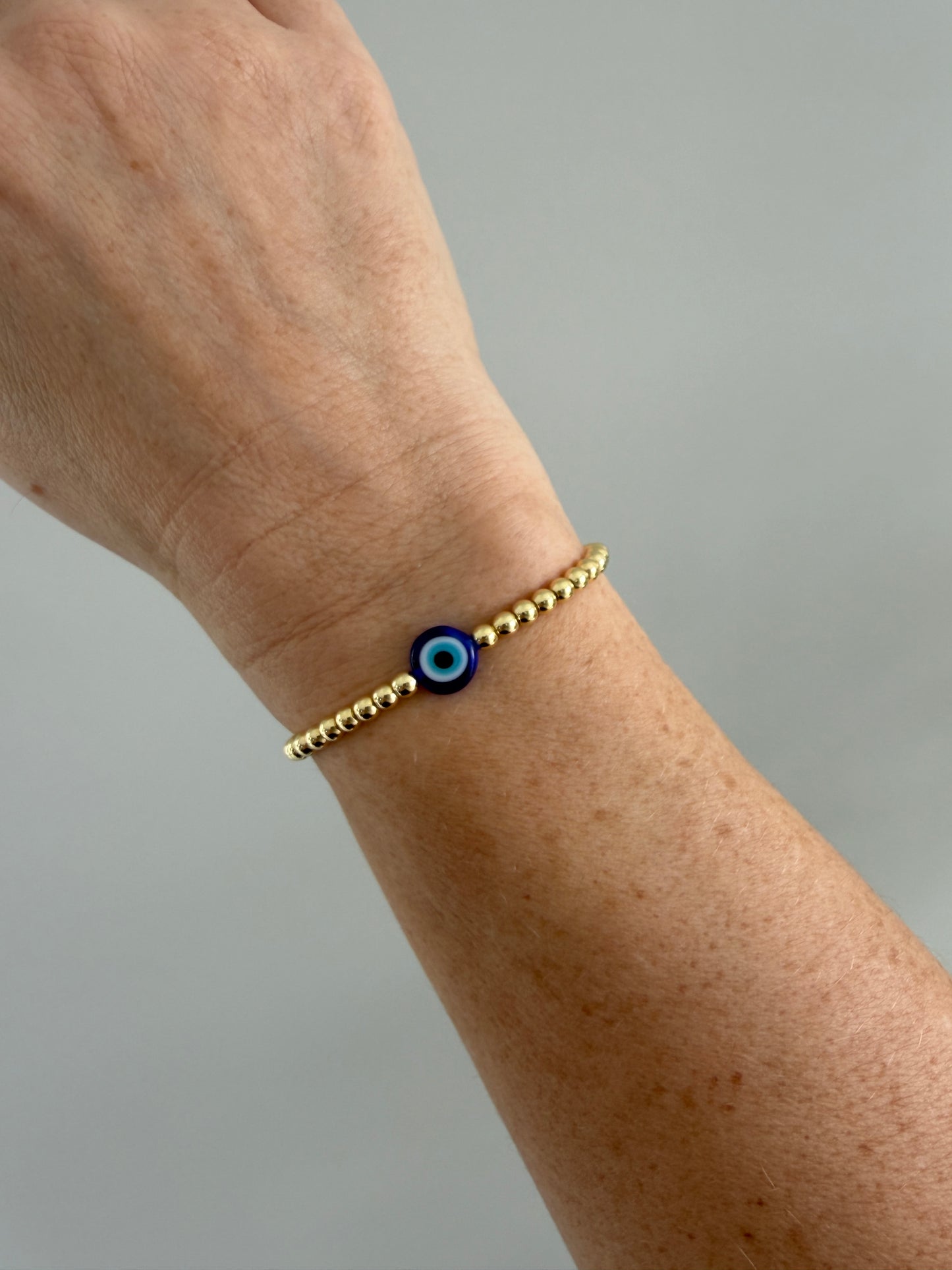 Gold bracelet with a blue eye charm on a wrist against a gray background