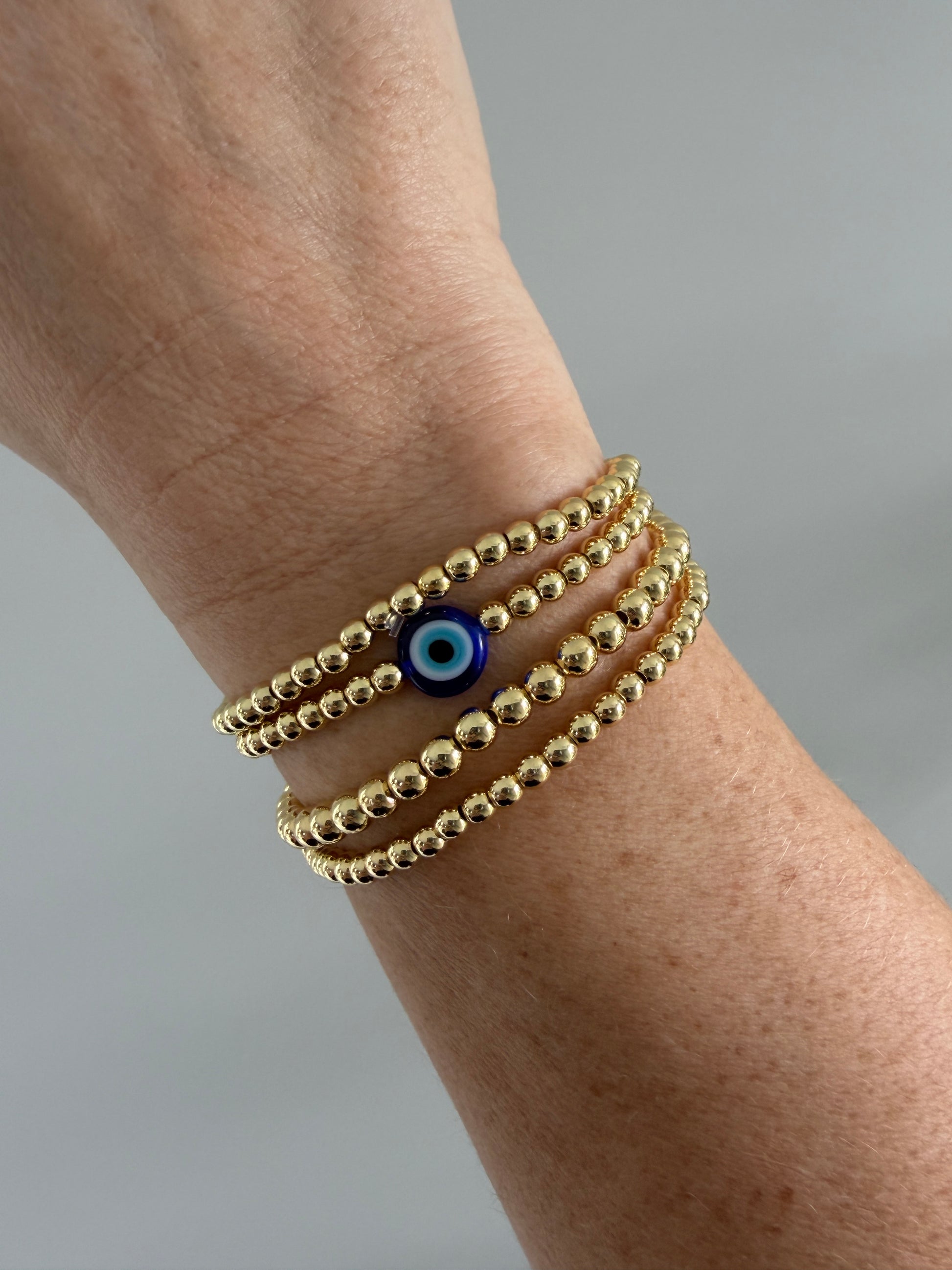 Gold-filled evil eye bracelet stacked with minimalist gold bracelets