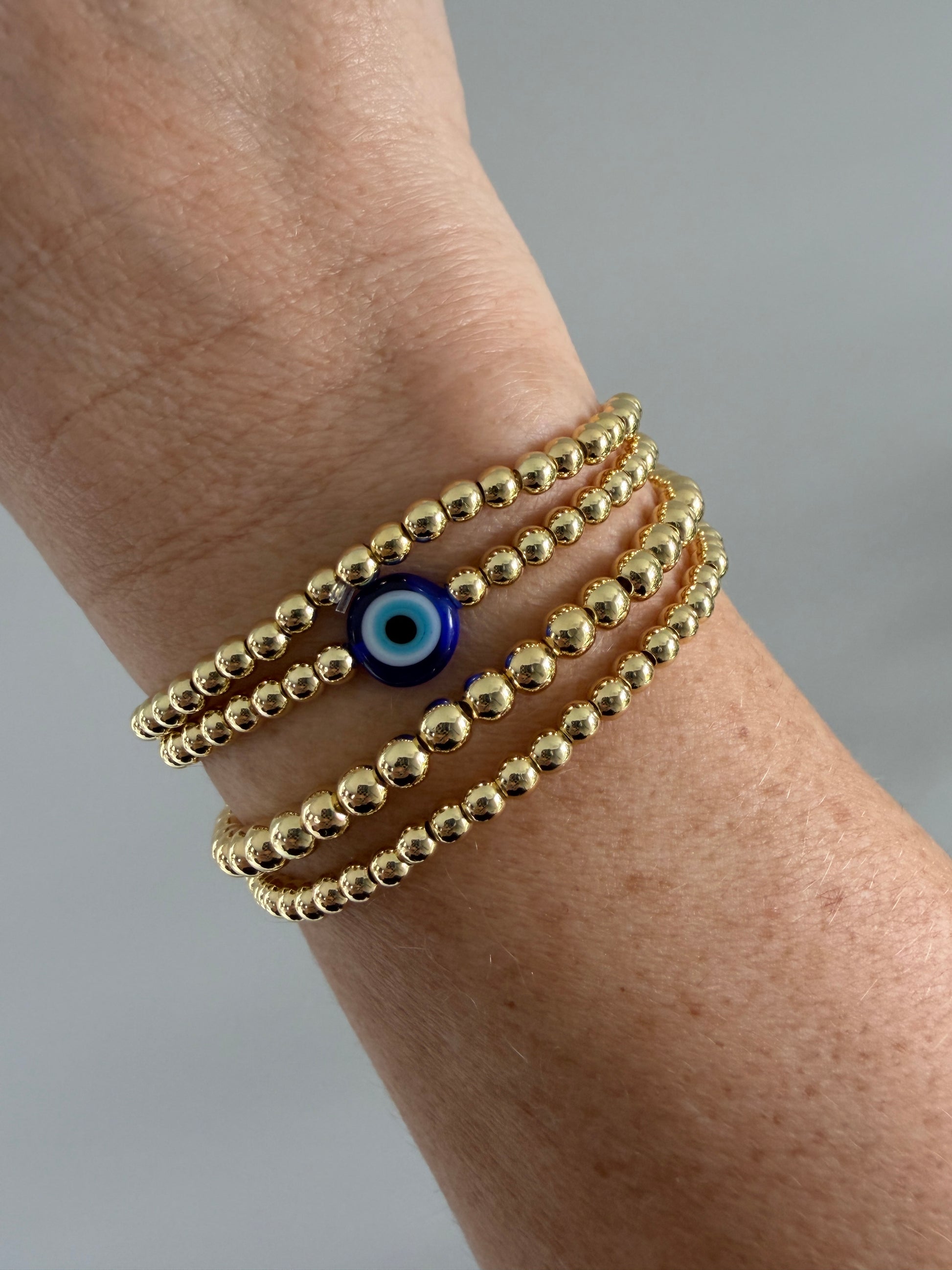 Gold-filled evil eye bracelet stacked with minimalist gold bracelets