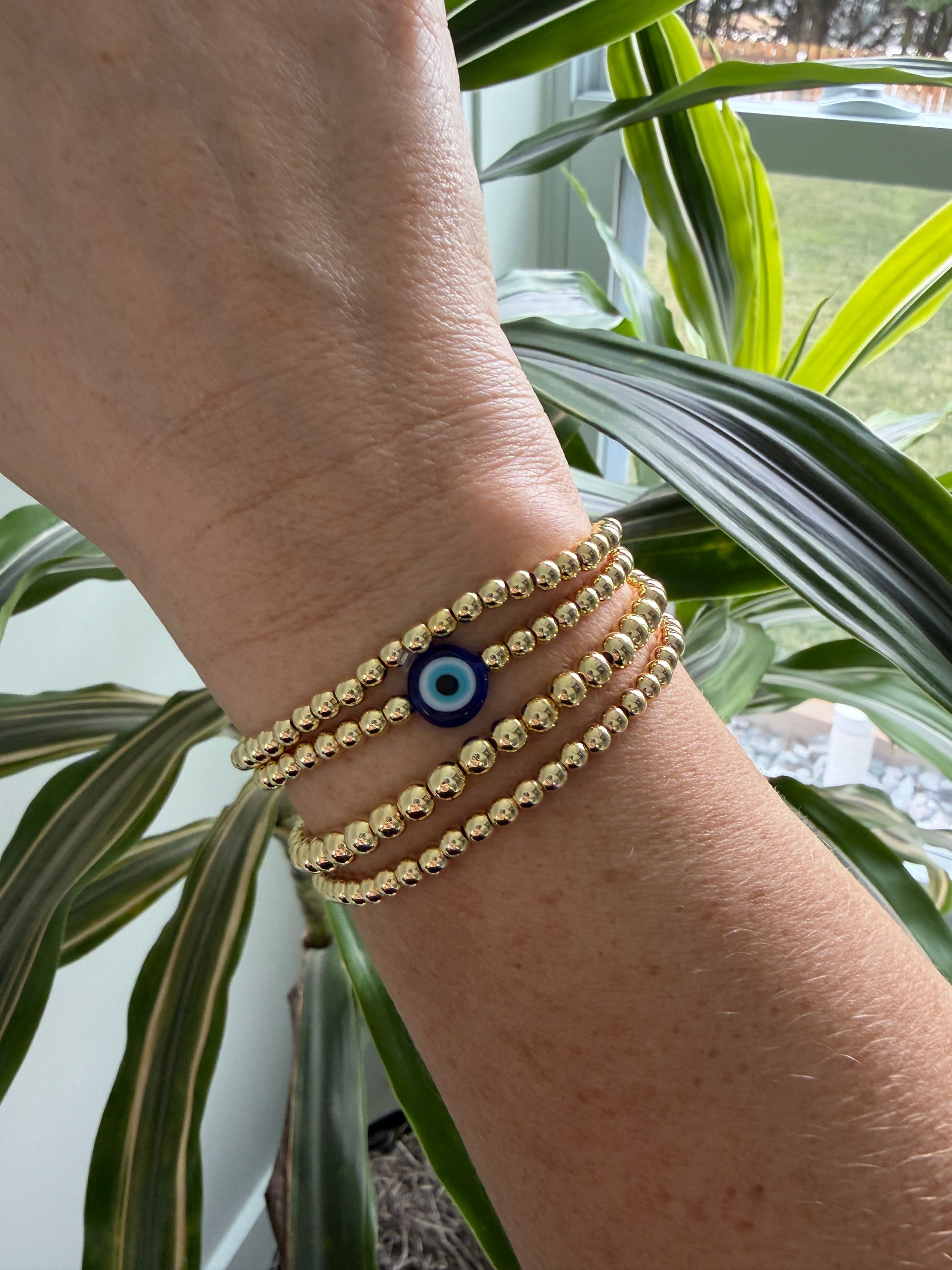 Gold-filled evil eye bracelet stacked with minimalist gold bracelets