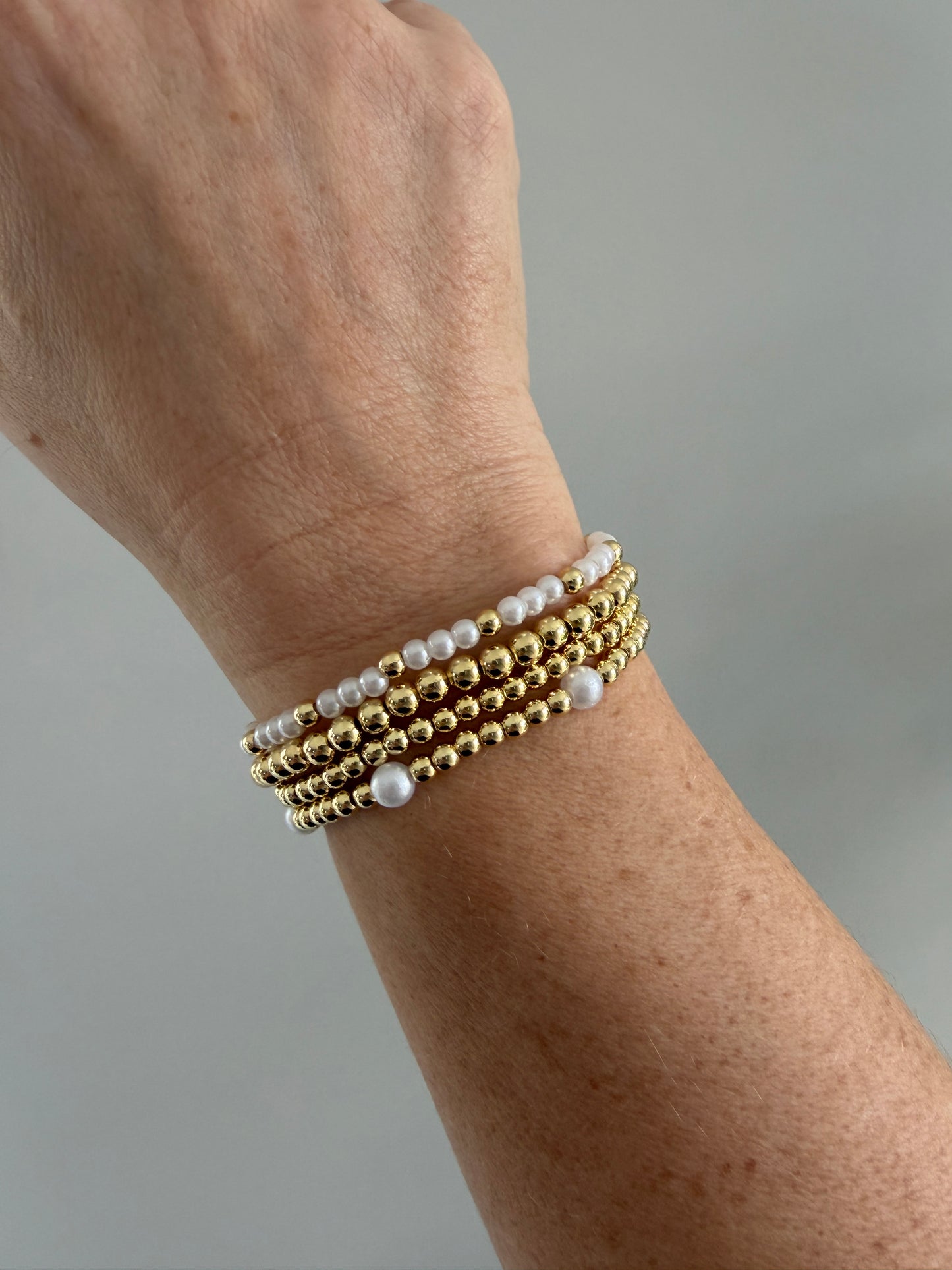 Gold and pearl beaded bracelets on a wrist against a neutral background