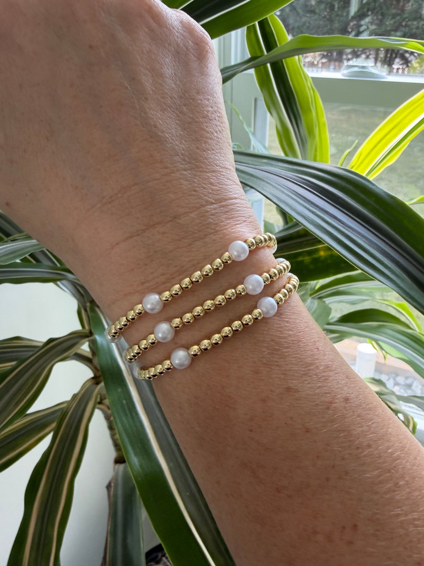 Close-up of a wrist wearing gold and pearl beaded bracelets with a natural background