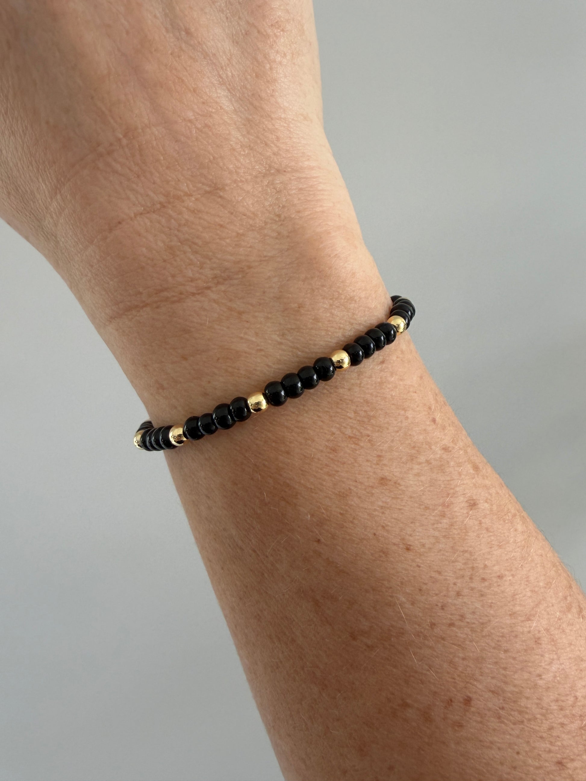 Gold-filled beaded bracelet with black beads stacked with minimalist gold bracelets
