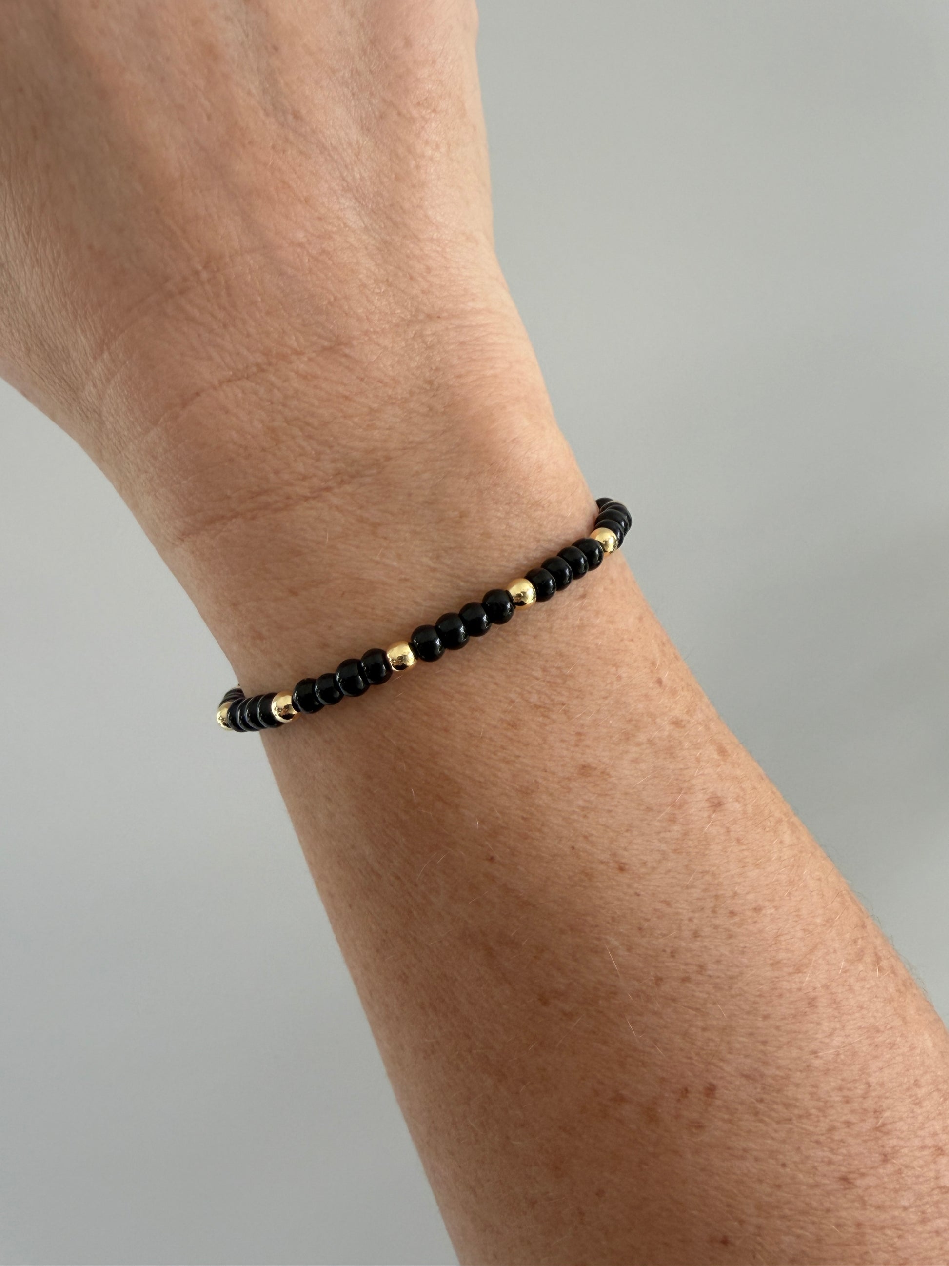 Gold-filled beaded bracelet with black beads stacked with minimalist gold bracelets