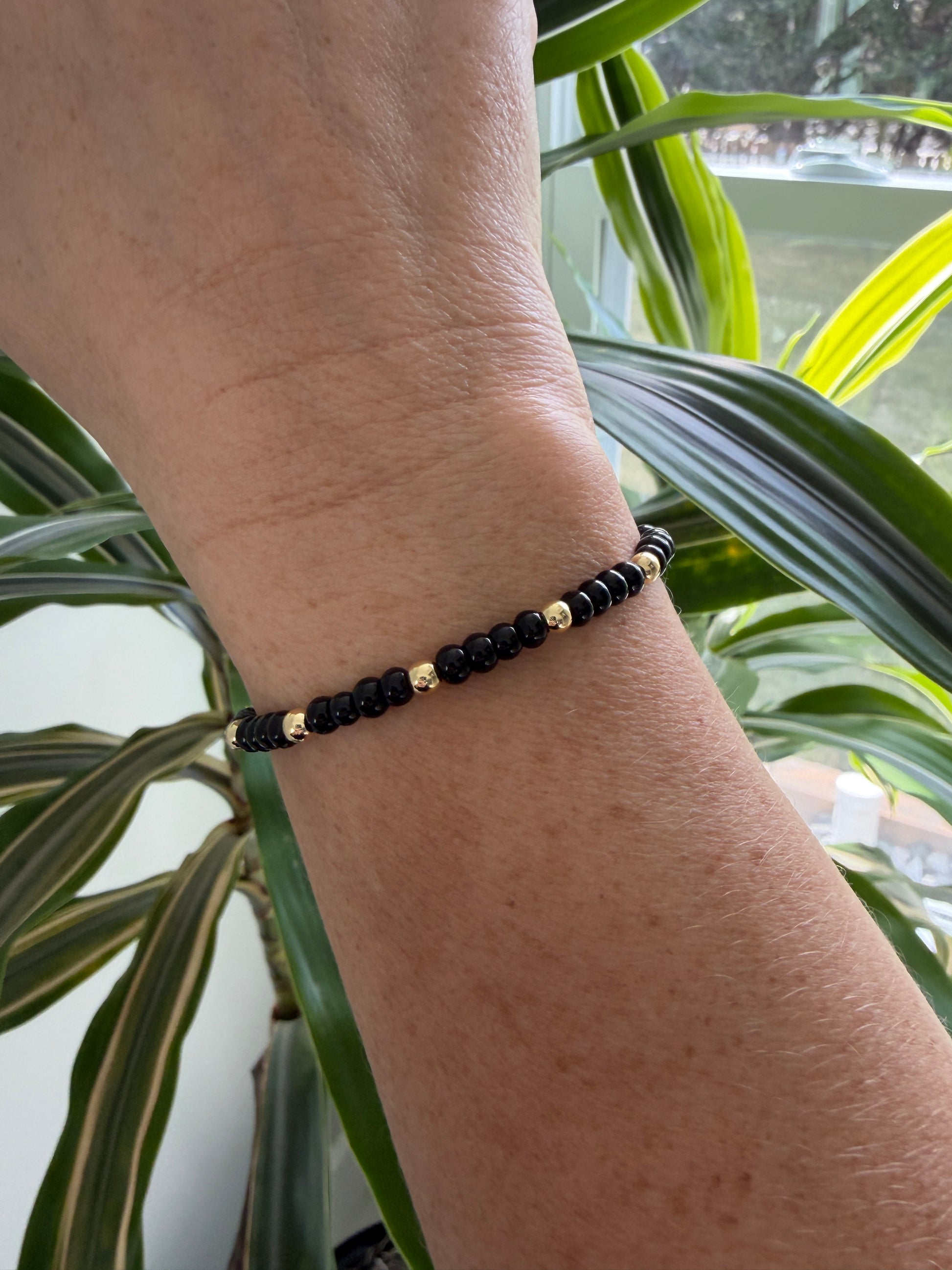 Gold-filled beaded bracelet with black beads stacked with minimalist gold bracelets