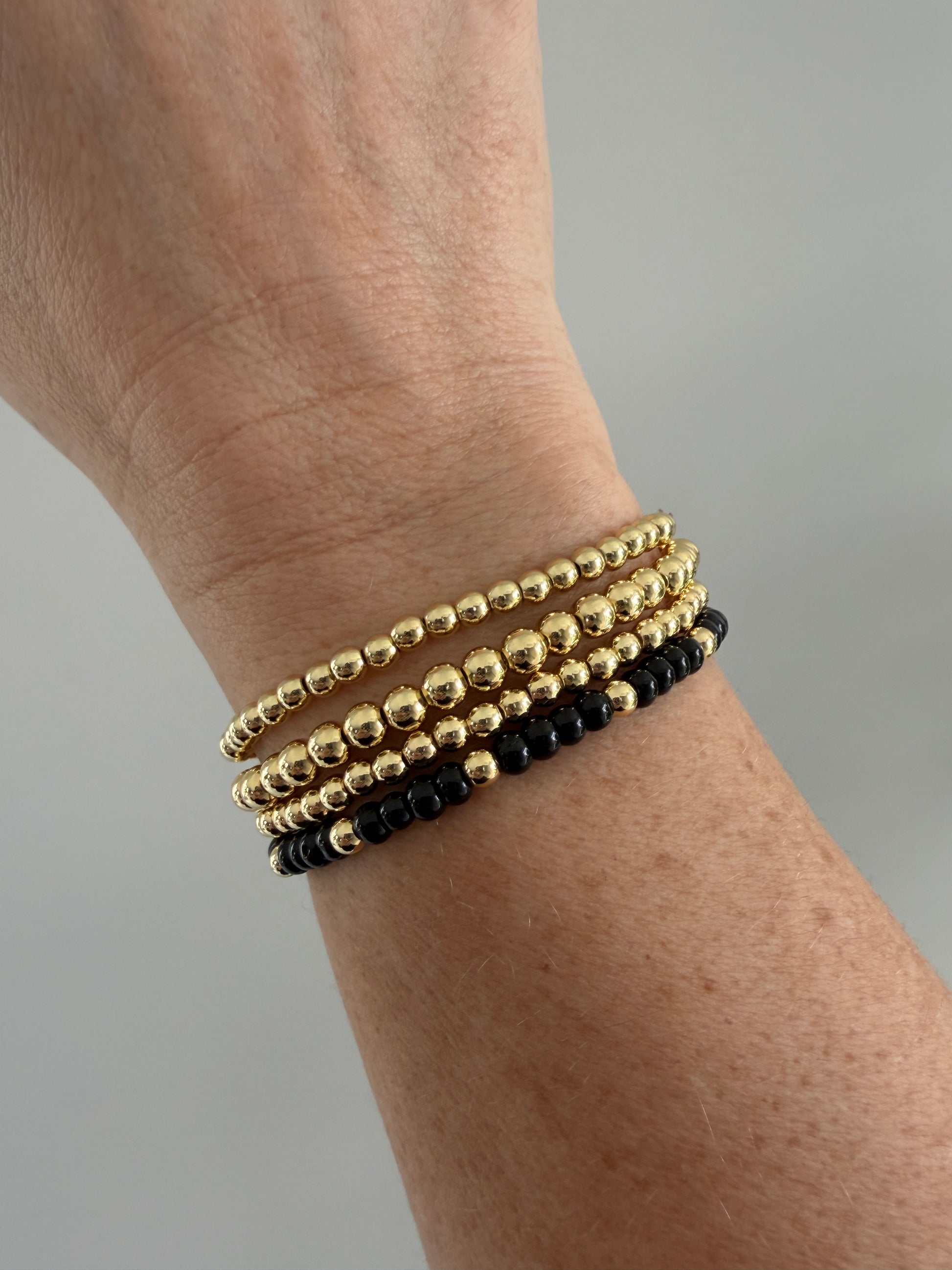 Gold-filled beaded bracelet with black beads stacked with minimalist gold bracelets