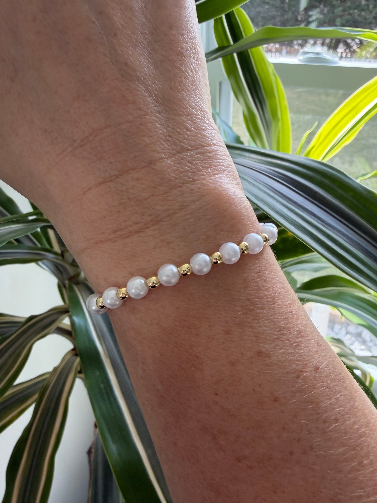 Pearl bracelet on a wrist with a plant in the background
