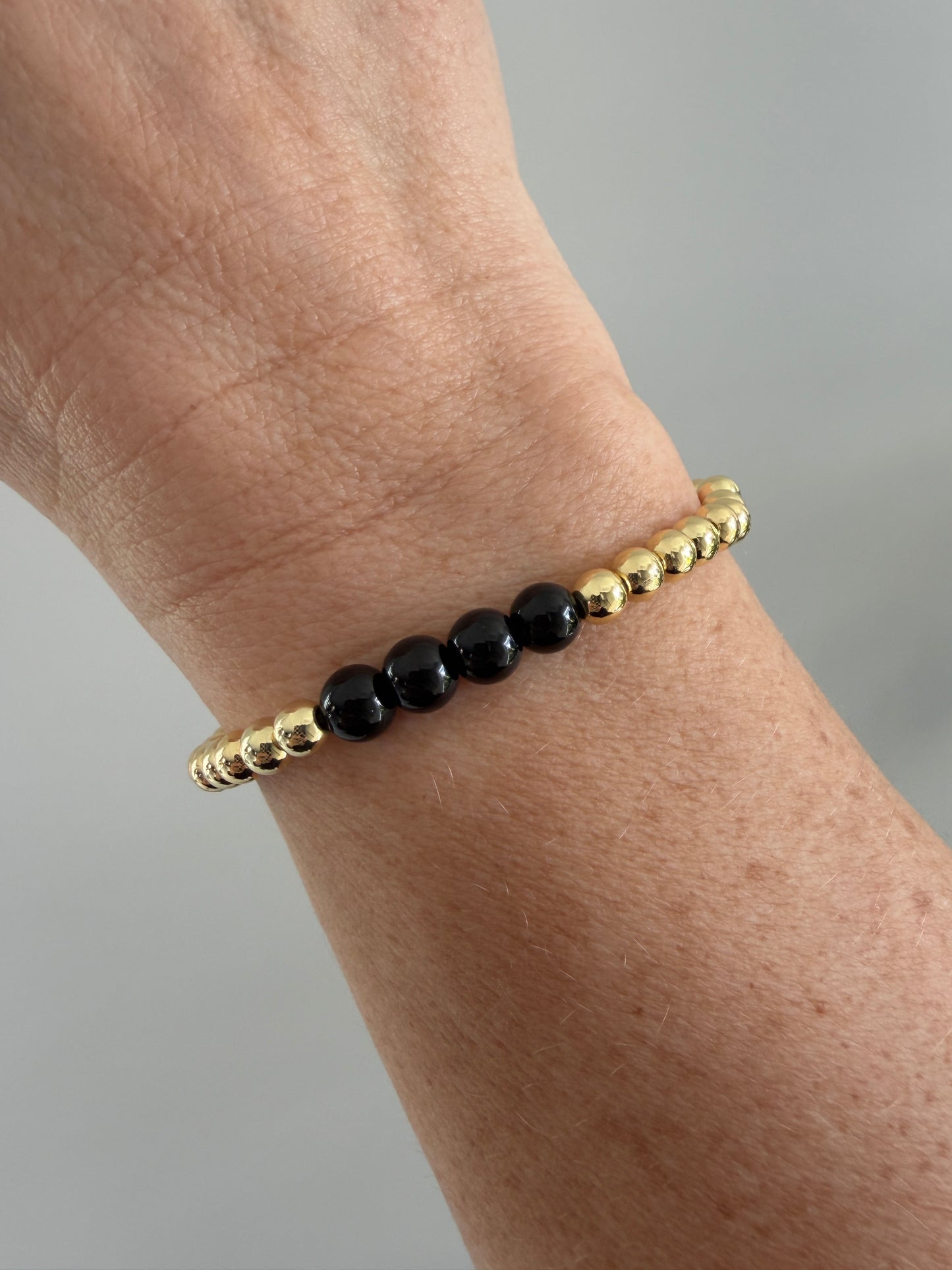 Bracelet with gold and black beads on a wrist against a neutral background