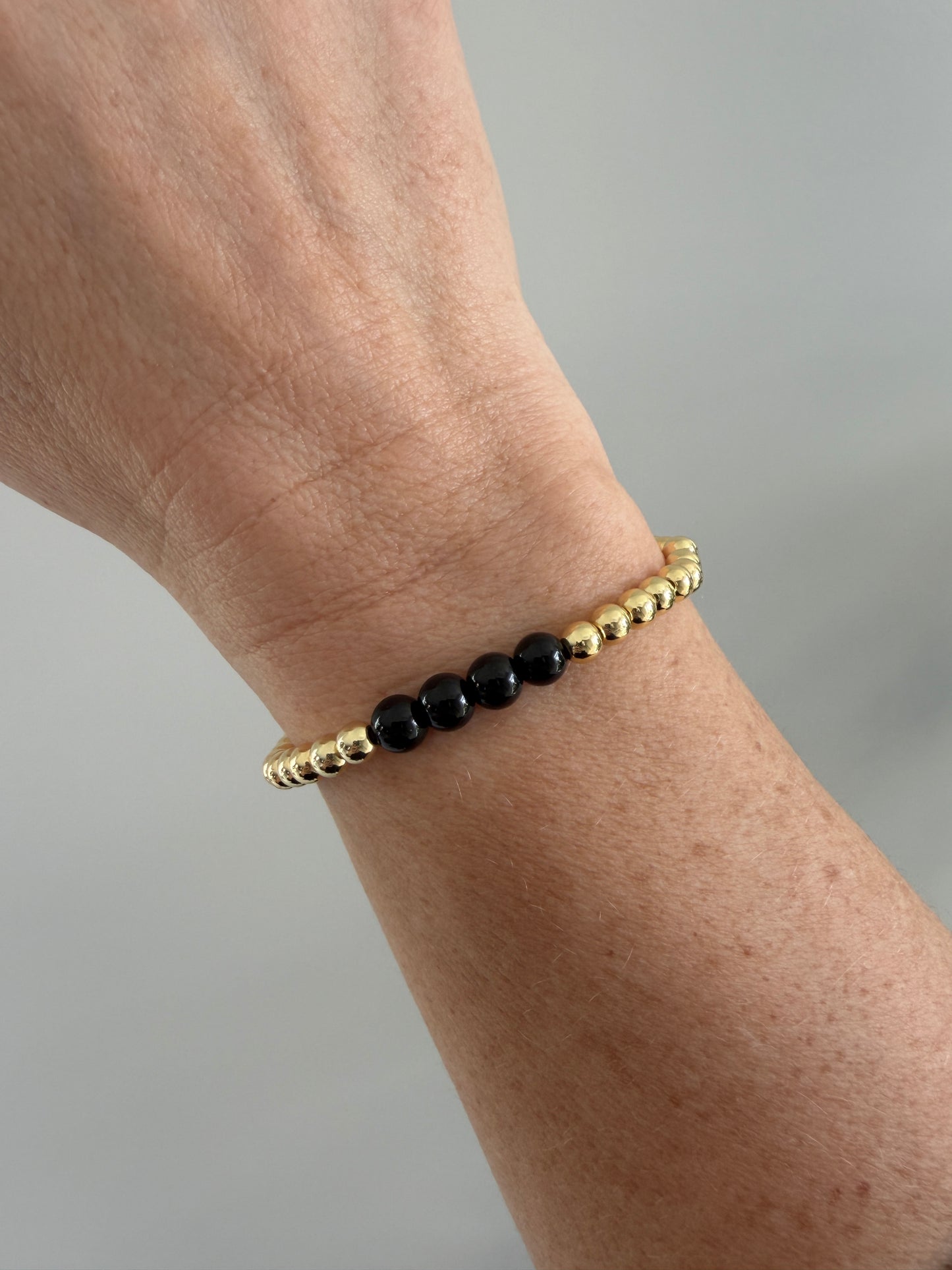 Gold and black beaded bracelet on a wrist against a neutral background