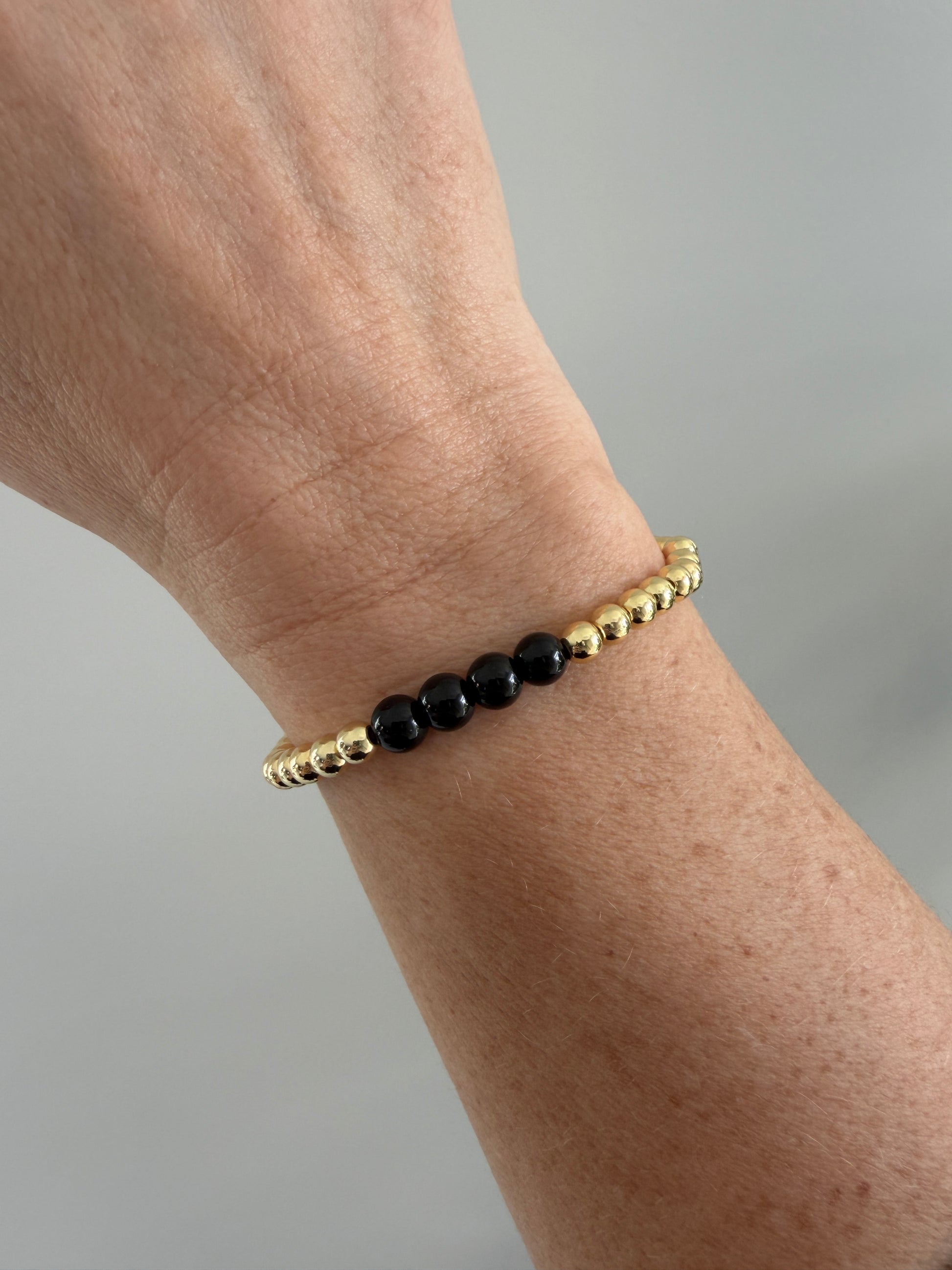 Gold and black beaded bracelet on a wrist against a neutral background