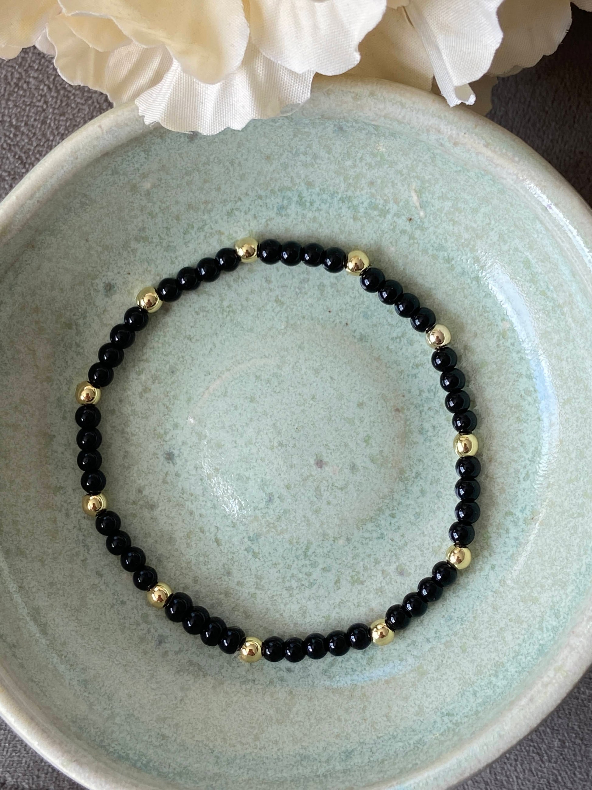 Black beaded bracelet with gold accents on a light blue ceramic plate.