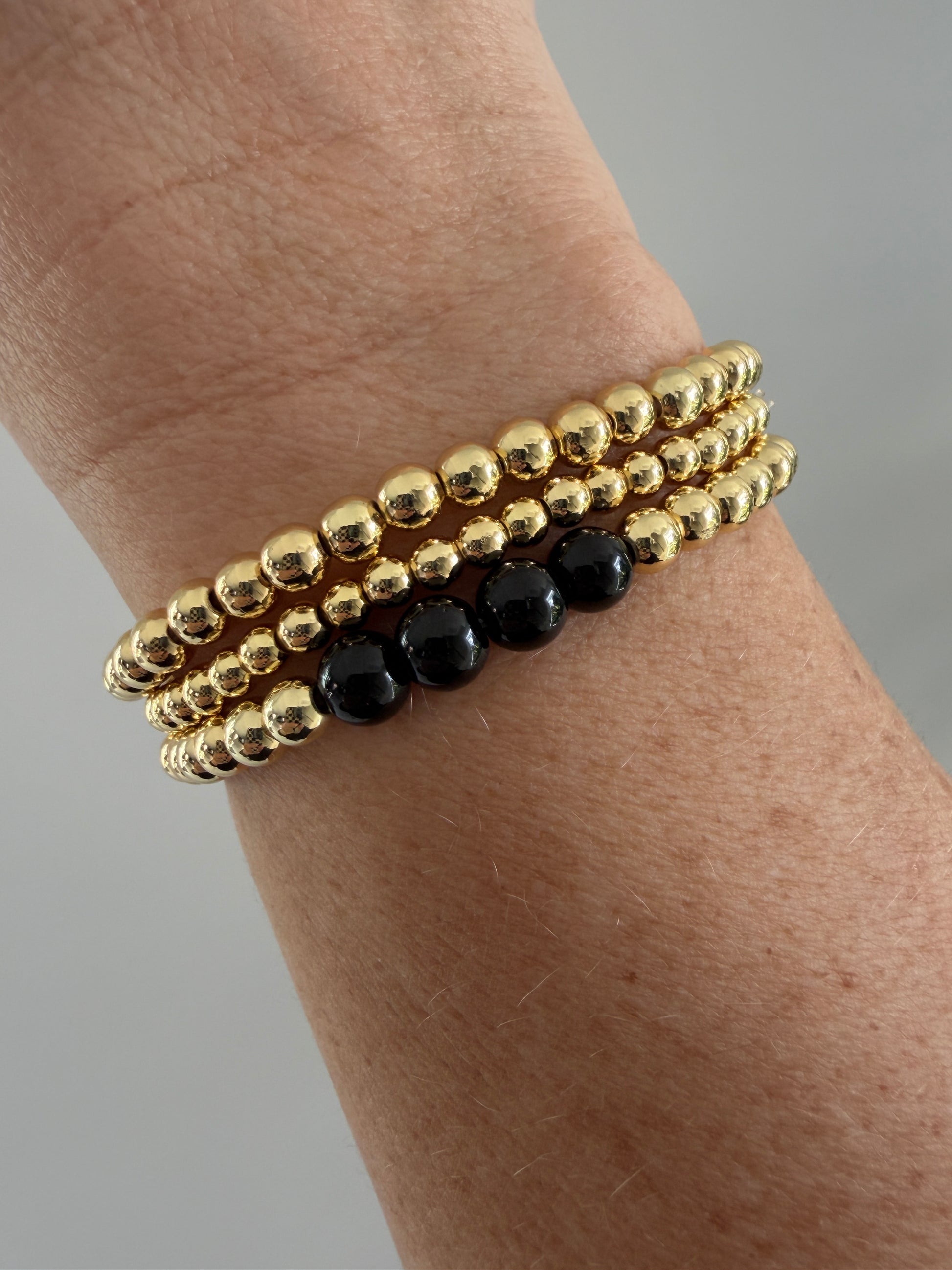 Gold beaded bracelet with black beads on a wrist against a neutral background