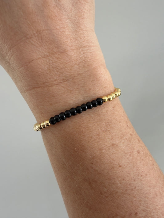Black beaded bracelet with gold accents on a wrist against a neutral background