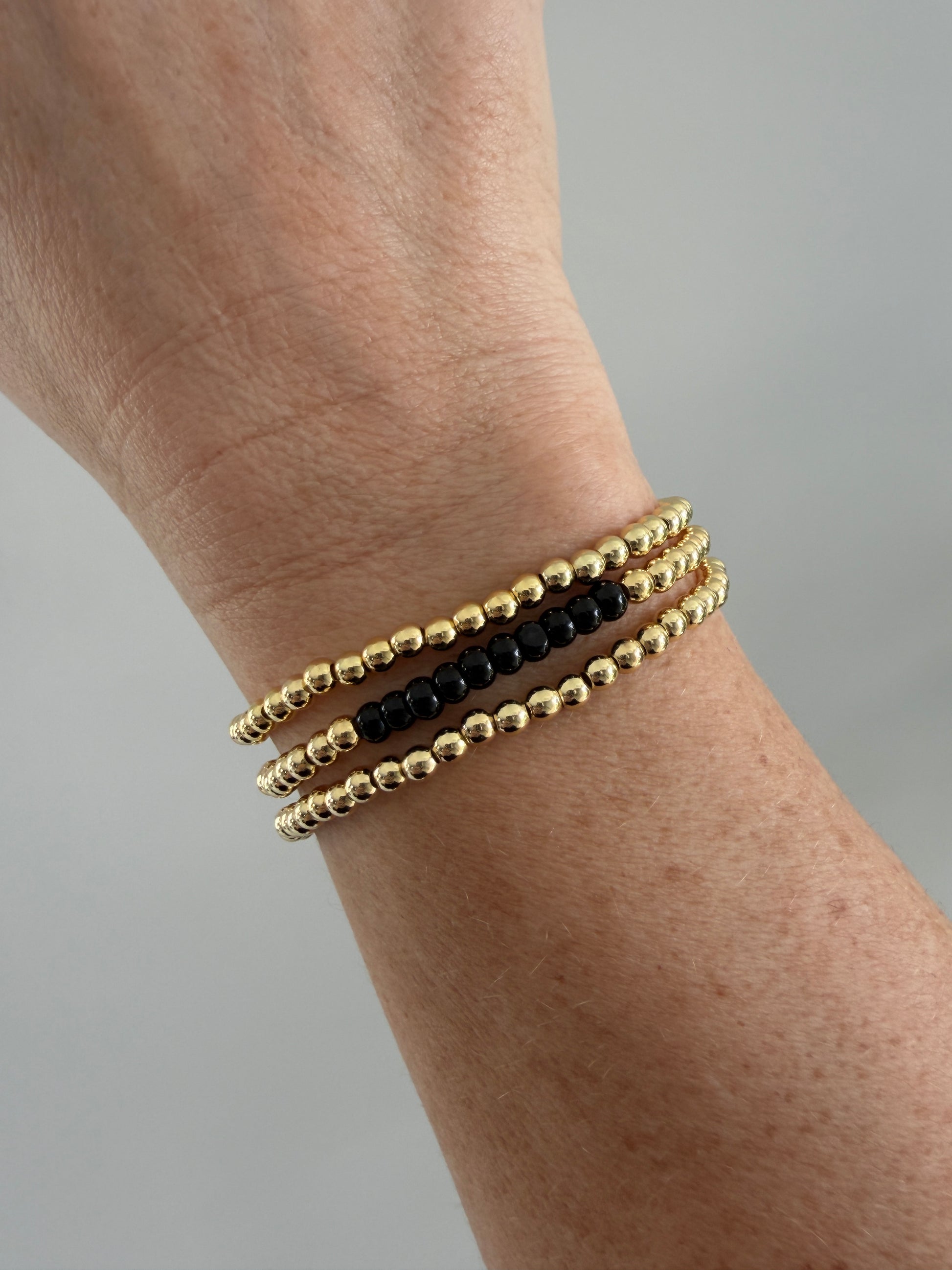 Gold and black beaded bracelets on a wrist against a gray background