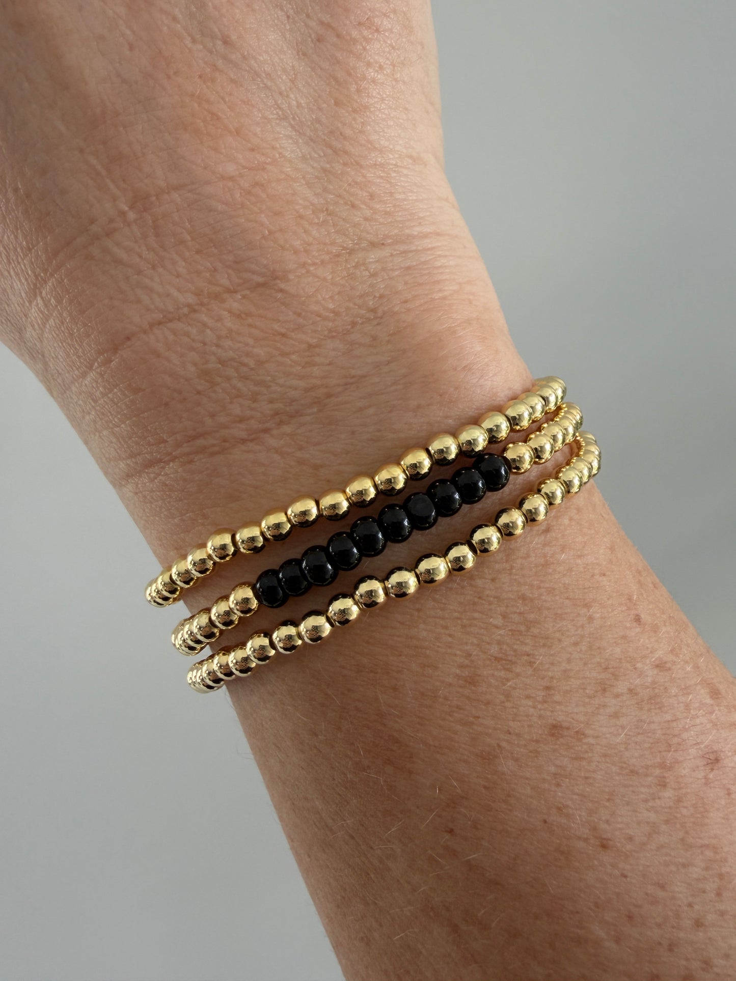 Gold and black beaded bracelets on a wrist against a neutral background