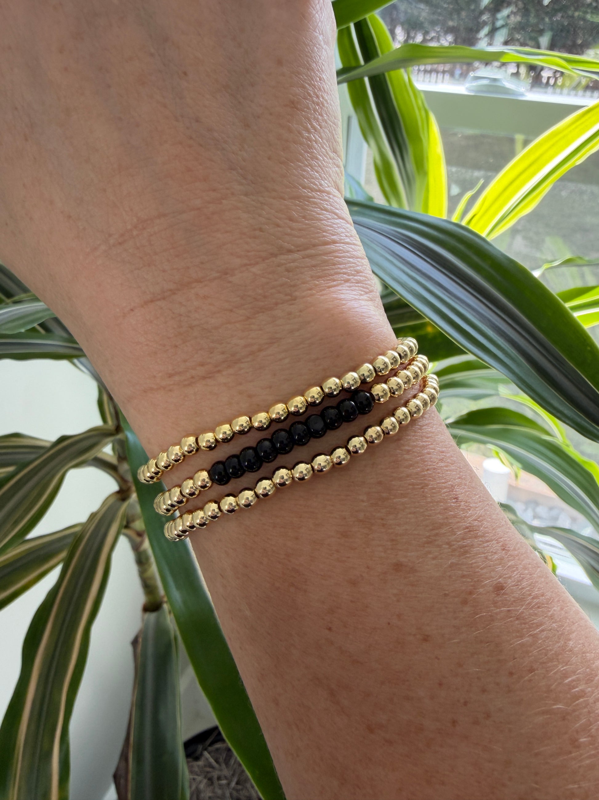 Close-up of a wrist wearing two beaded bracelets with a plant in the background
