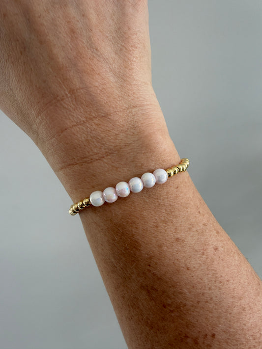 Pearl bracelet with gold accents on a wrist against a neutral background