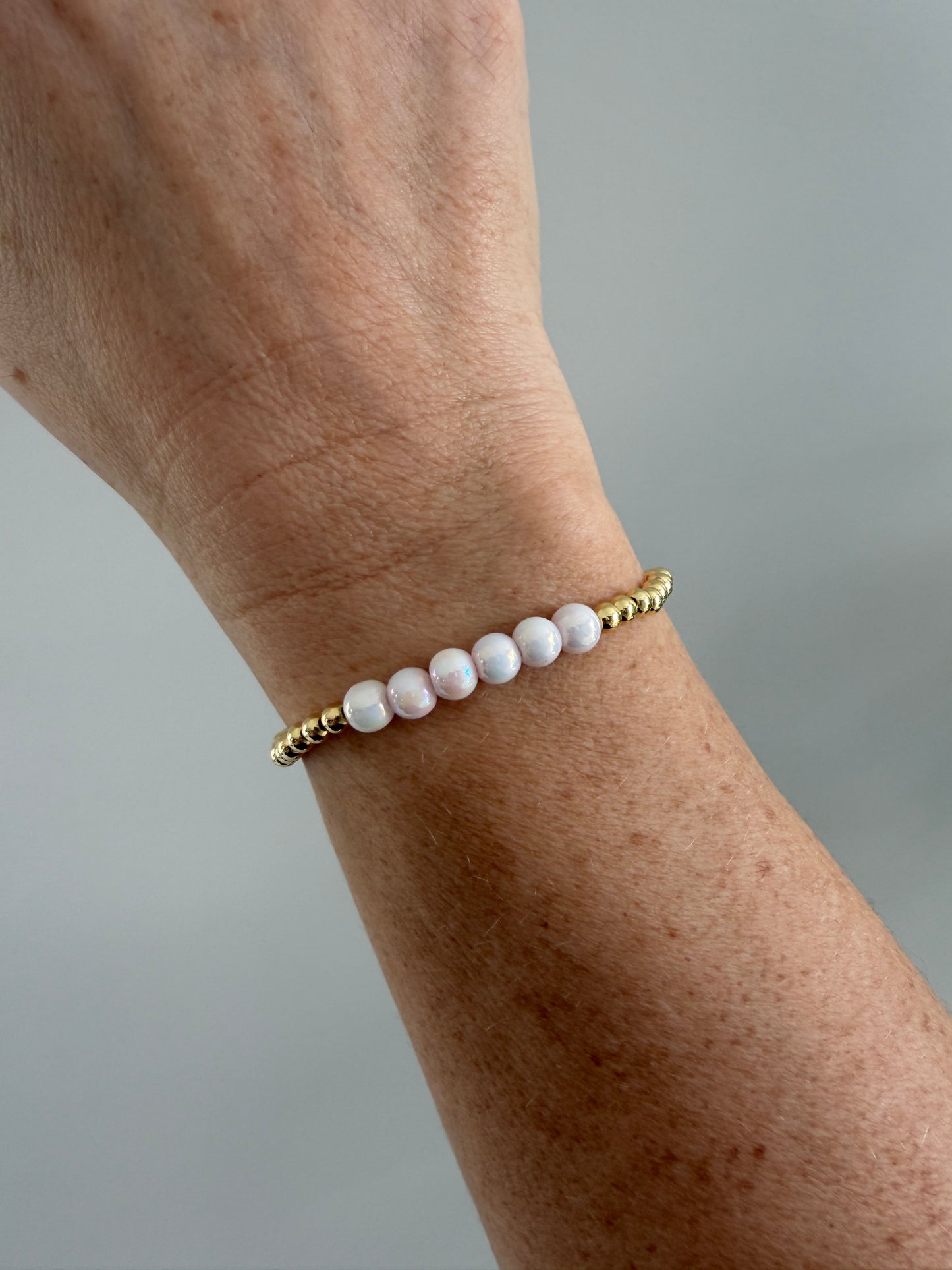 Close-up of a wrist wearing a bracelet with white beads and gold accents on a neutral background