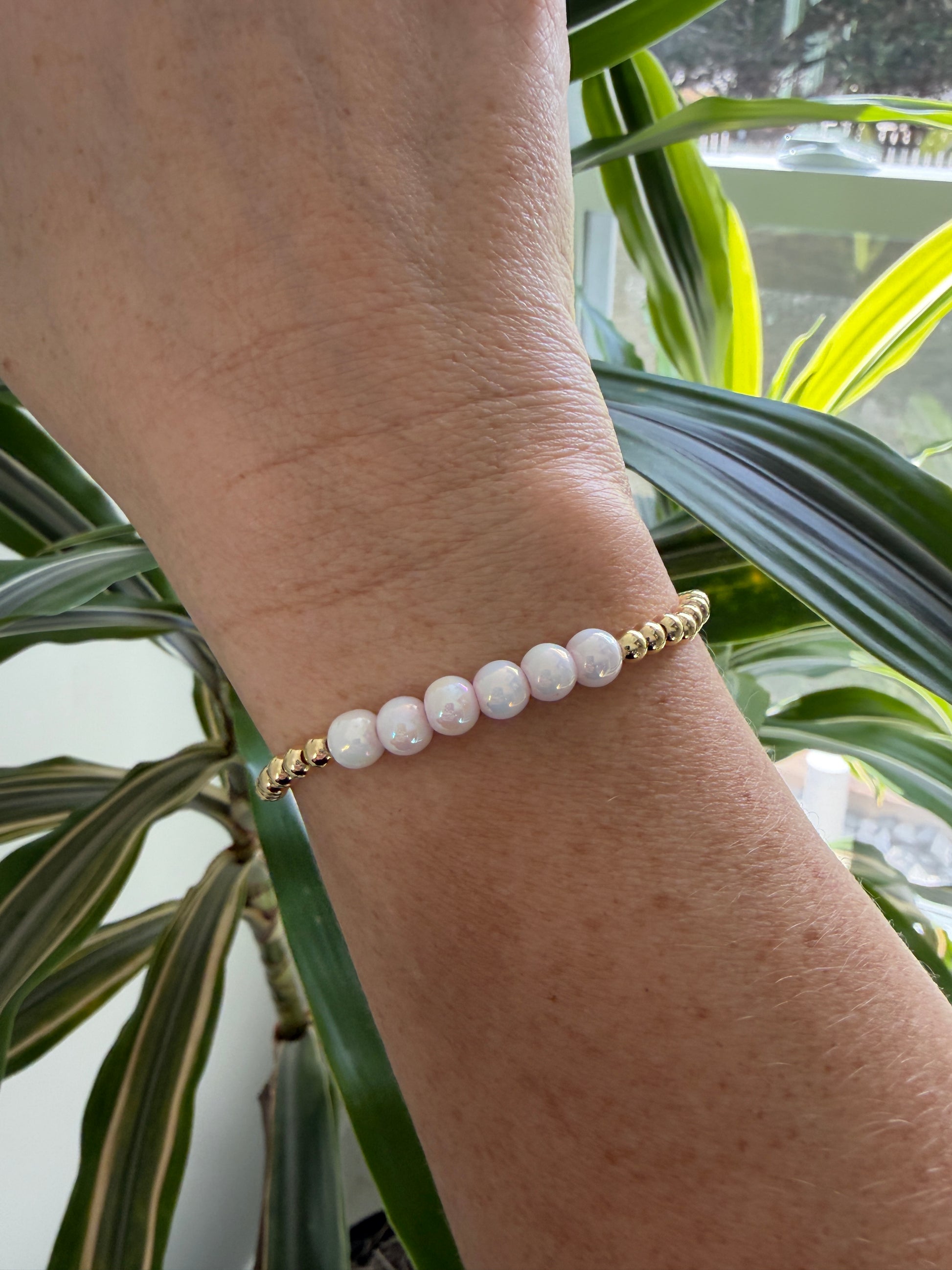 Bracelet with pink beads on a wrist against a plant background