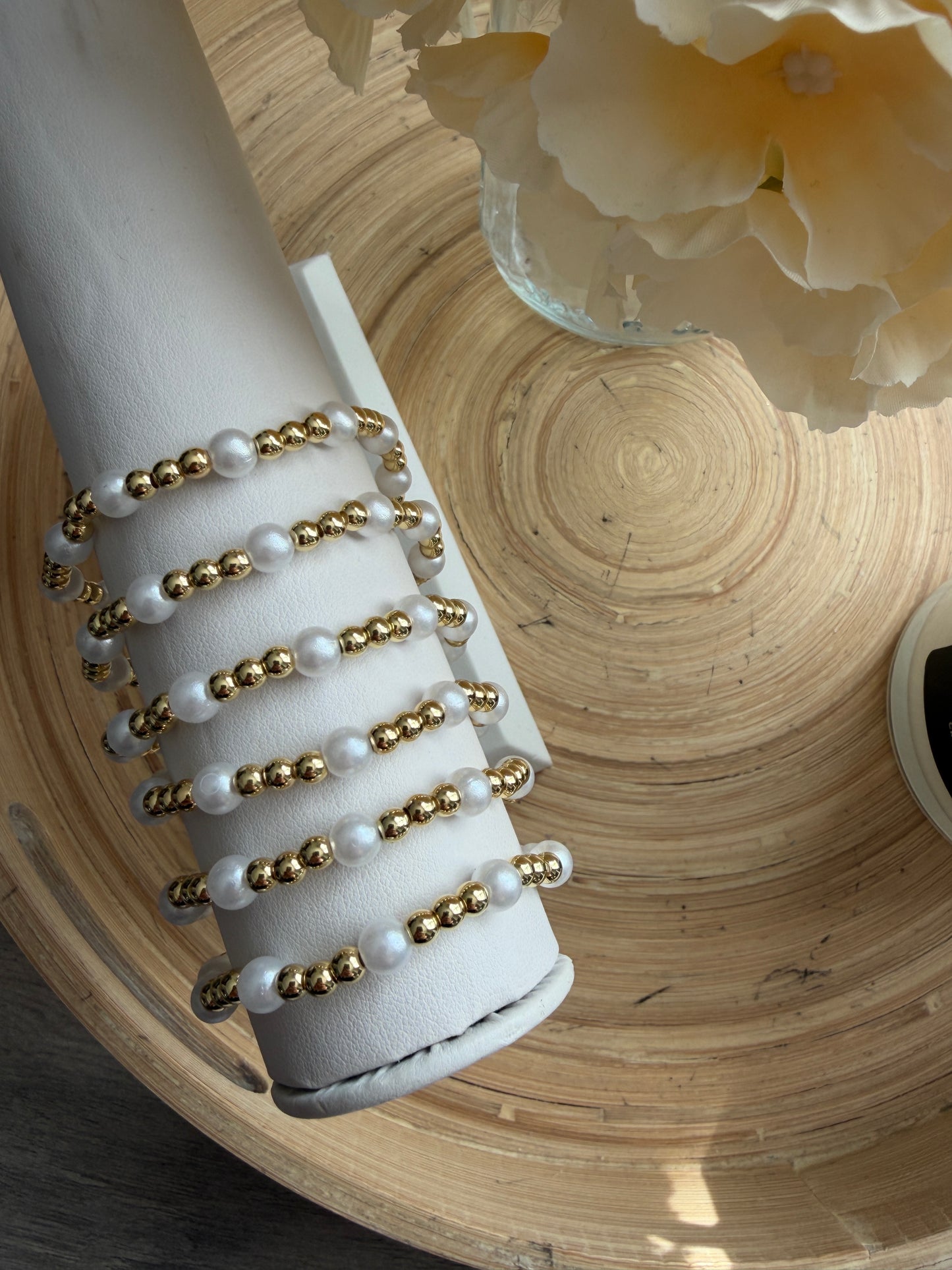 Set of pearl and gold beaded bracelets on a white cylindrical holder with a wooden surface background.