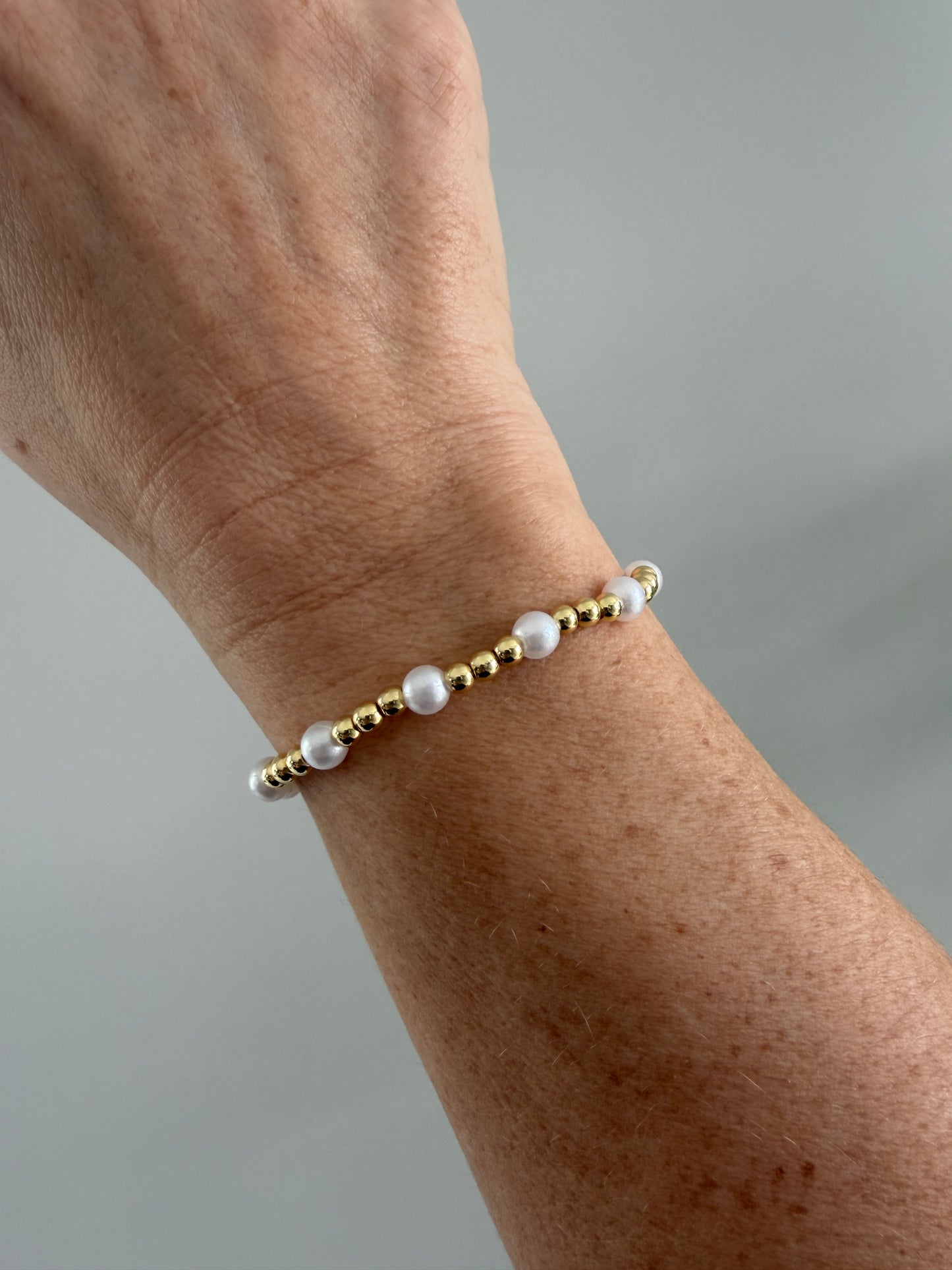 Gold and pearl bracelet on a wrist against a gray background