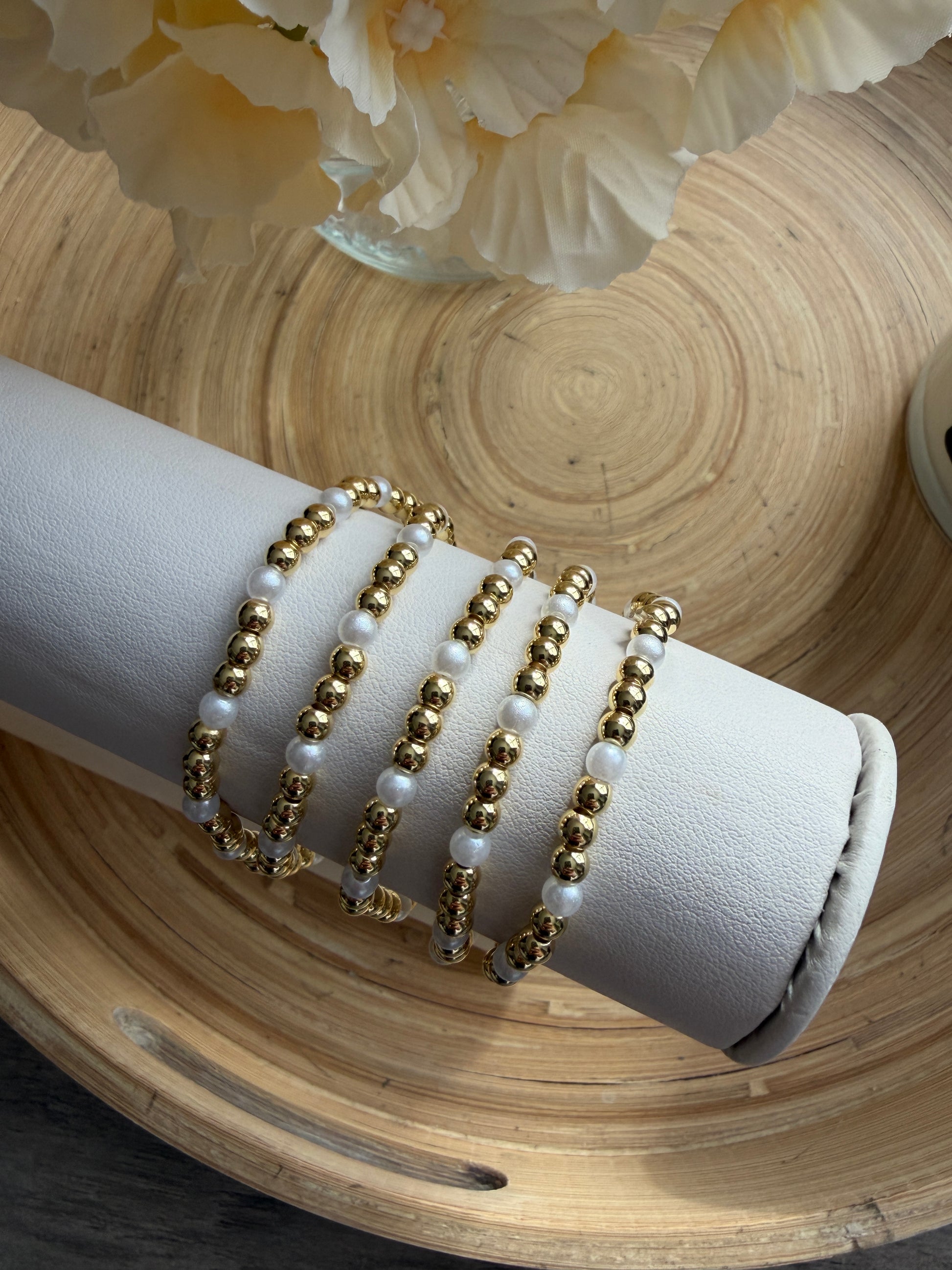 Set of gold and pearl beaded bracelets on a white cushion with a wooden background