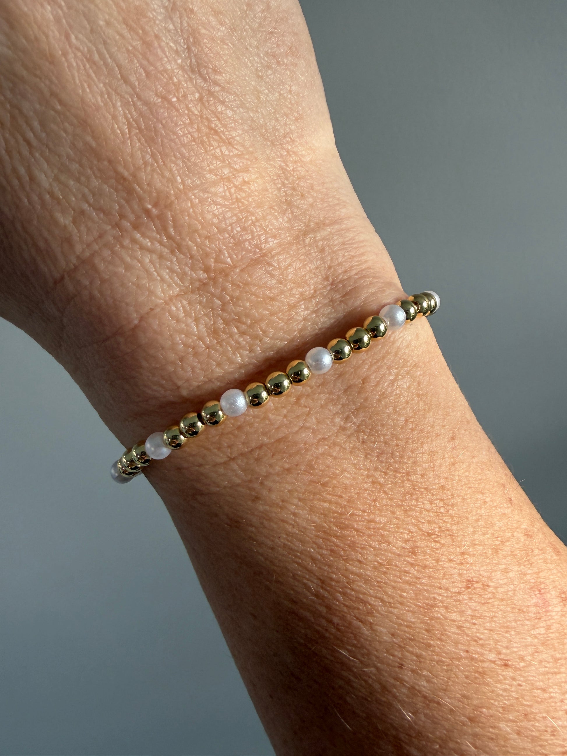 Gold and pearl beaded bracelet on a wrist against a gray background