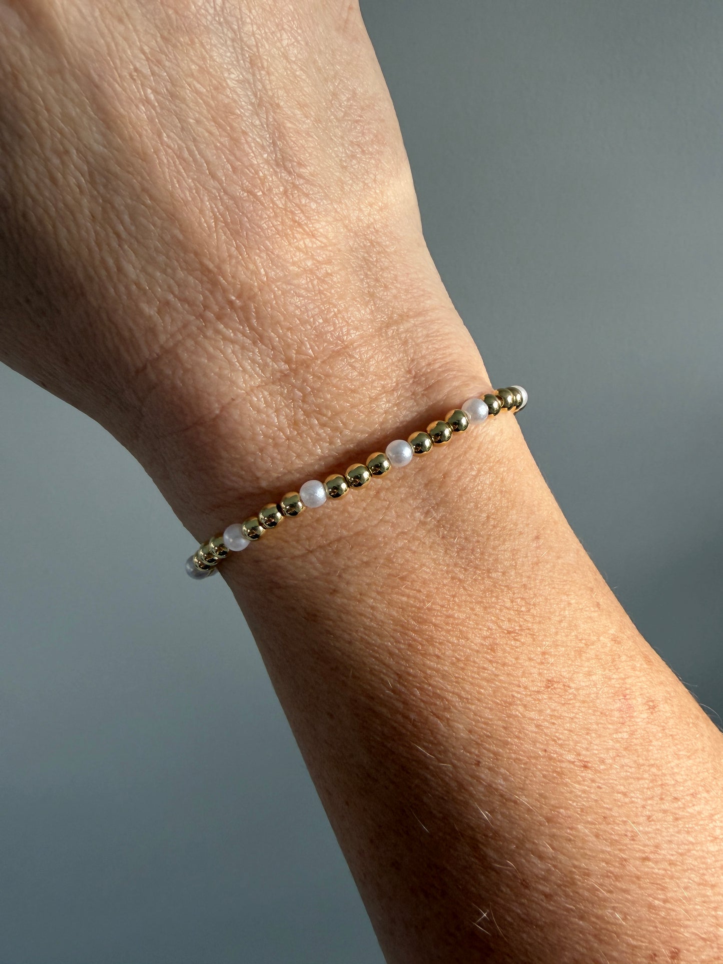 Bracelet with gold beads and pearls on a wrist against a neutral background