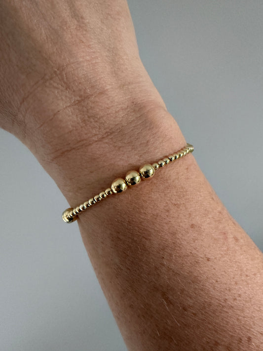 Gold beaded bracelet on a wrist against a gray background