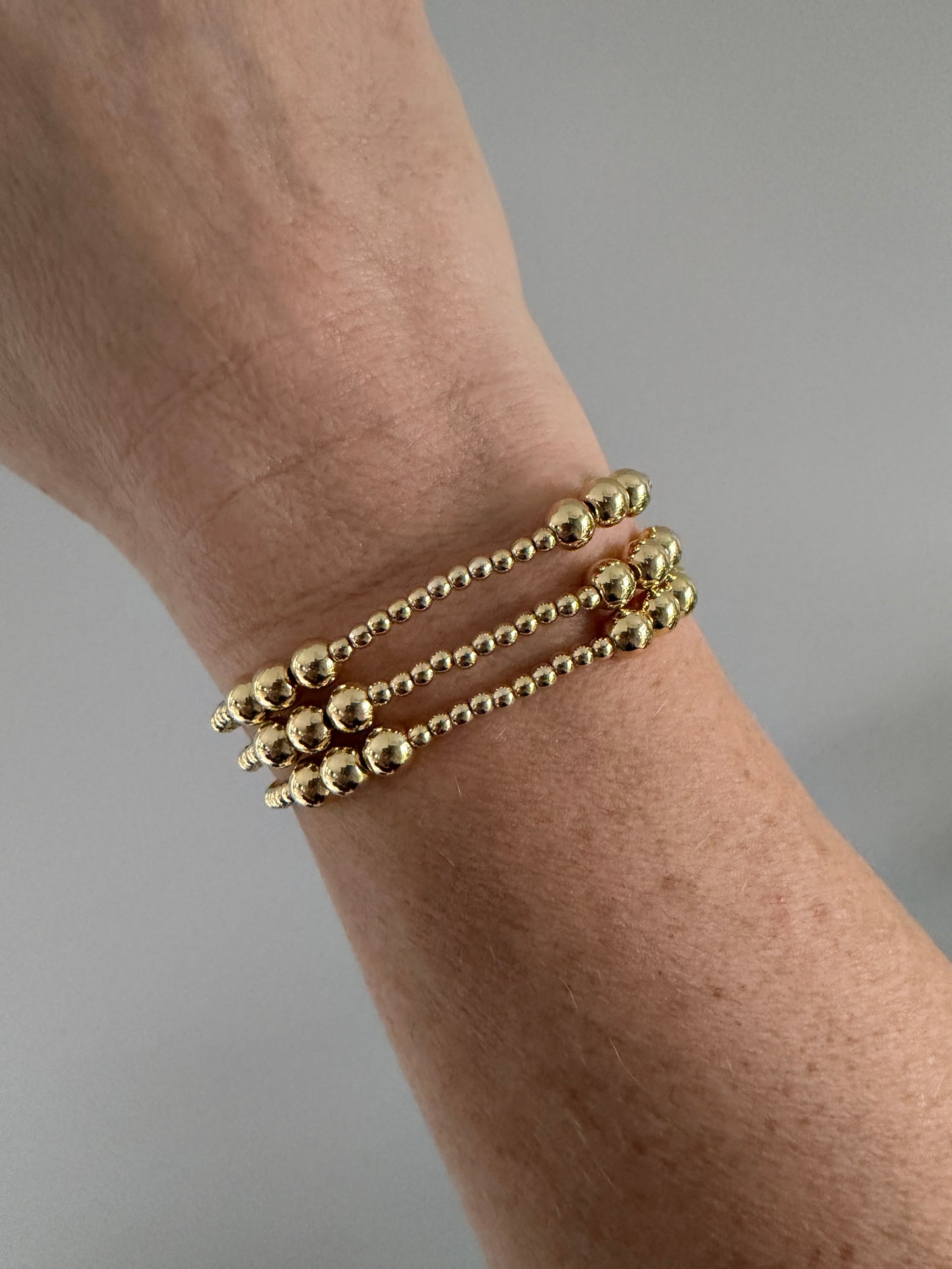 Gold beaded bracelet on a wrist against a neutral background