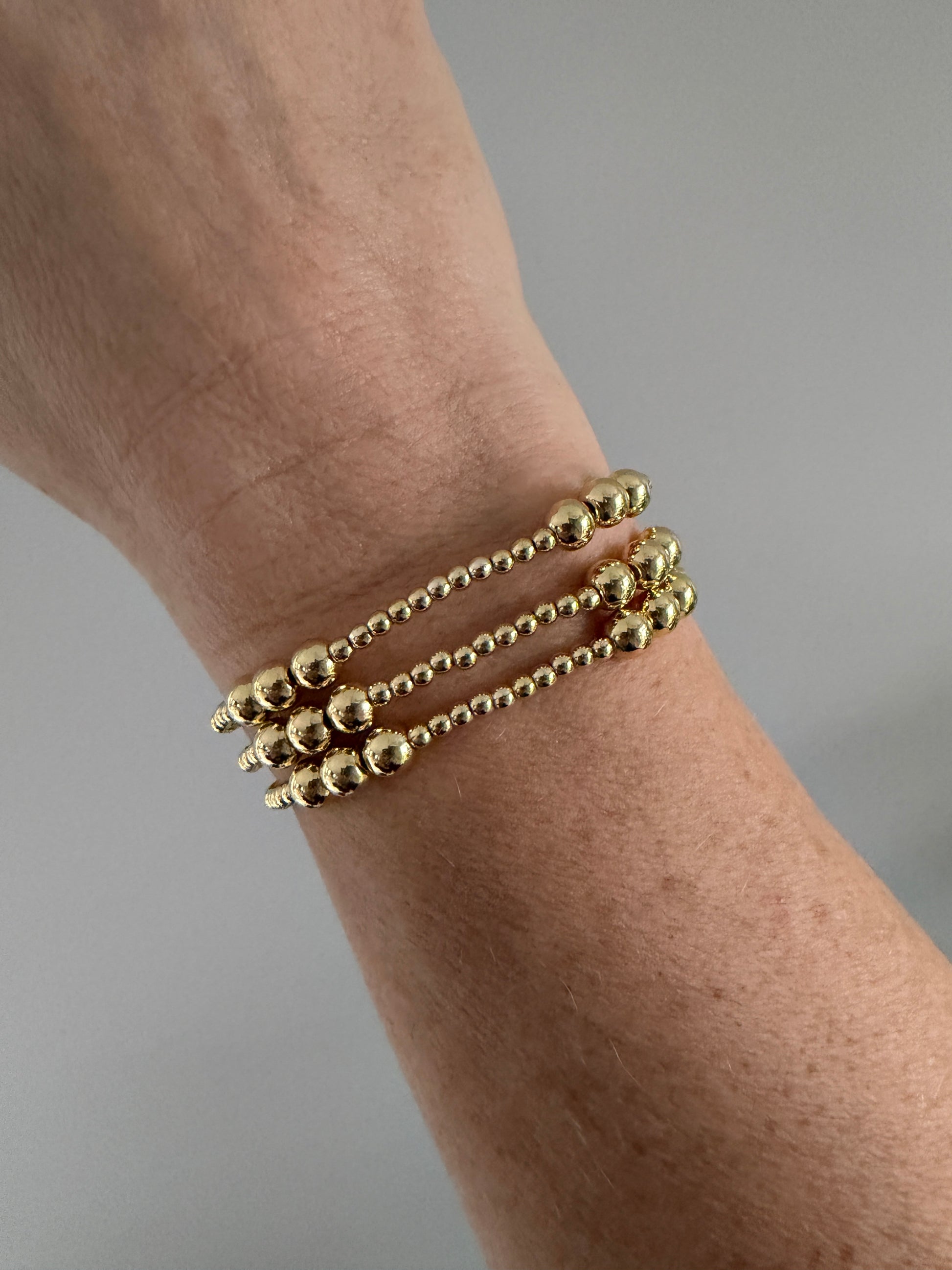 Gold beaded bracelet on a wrist against a neutral background