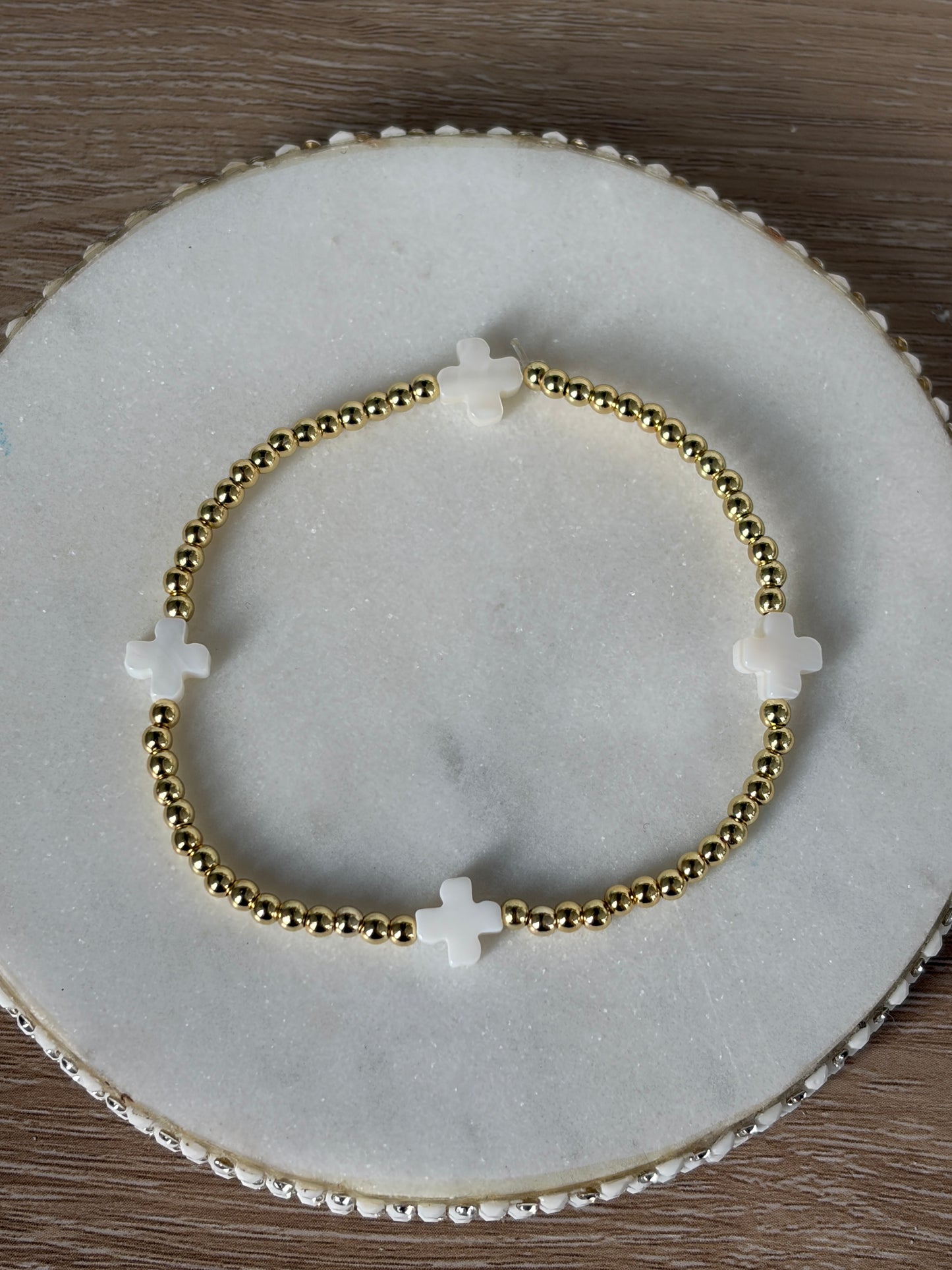 Gold beaded bracelet with white crosses on a marble surface