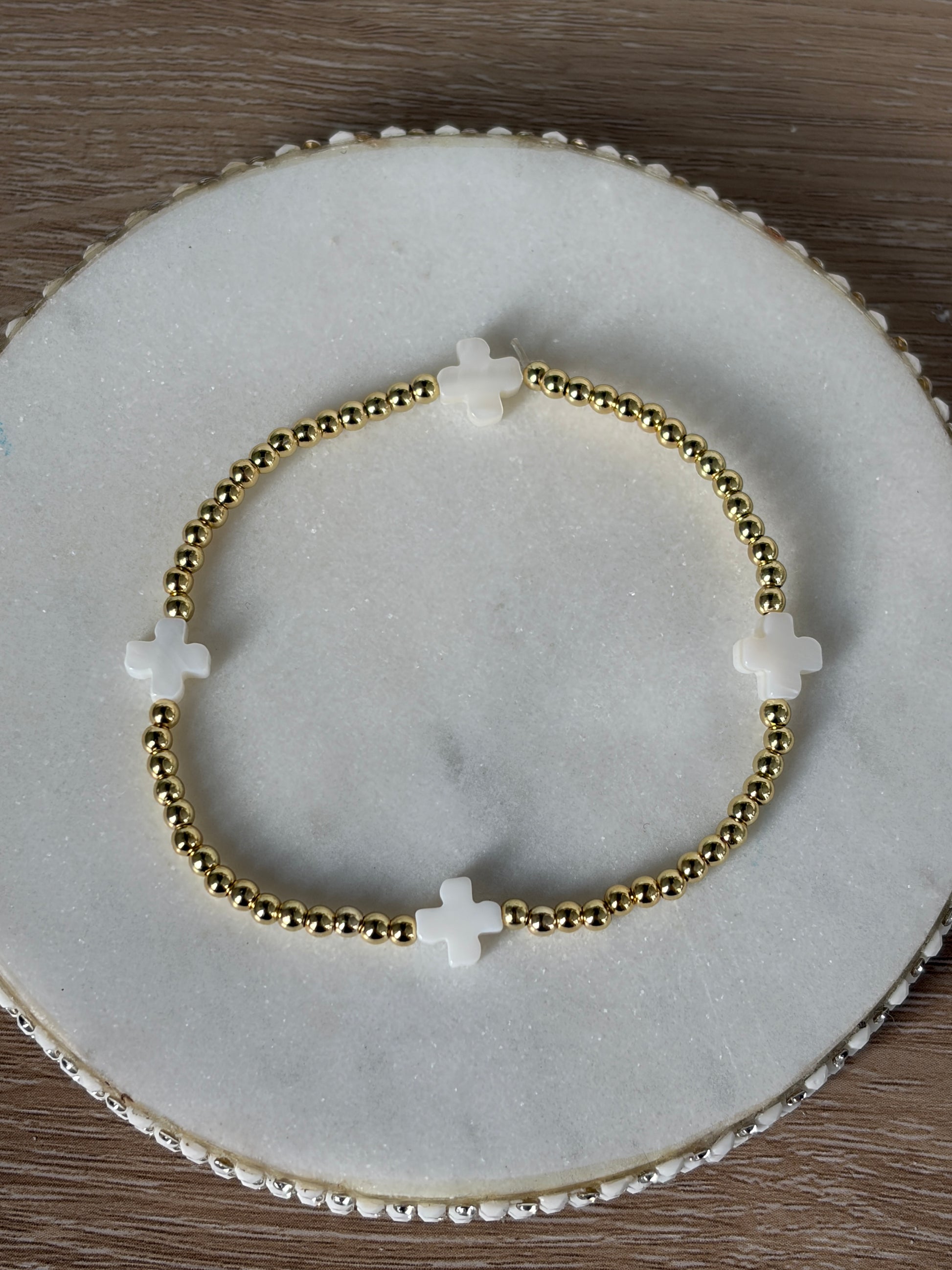 Gold beaded bracelet with white crosses on a marble surface