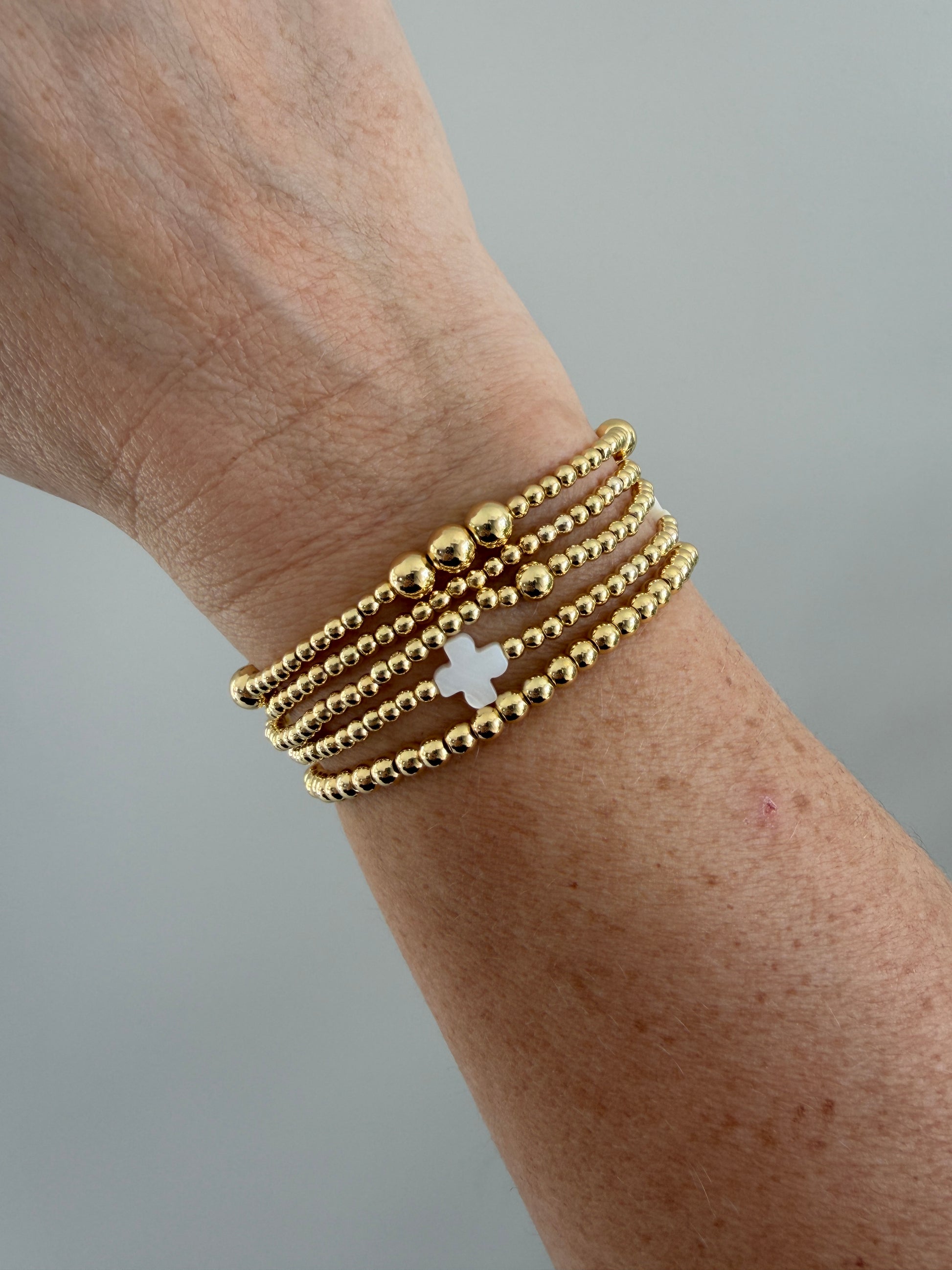 Stacked 18k gold-filled bracelets with white cross design, handmade beaded jewelry