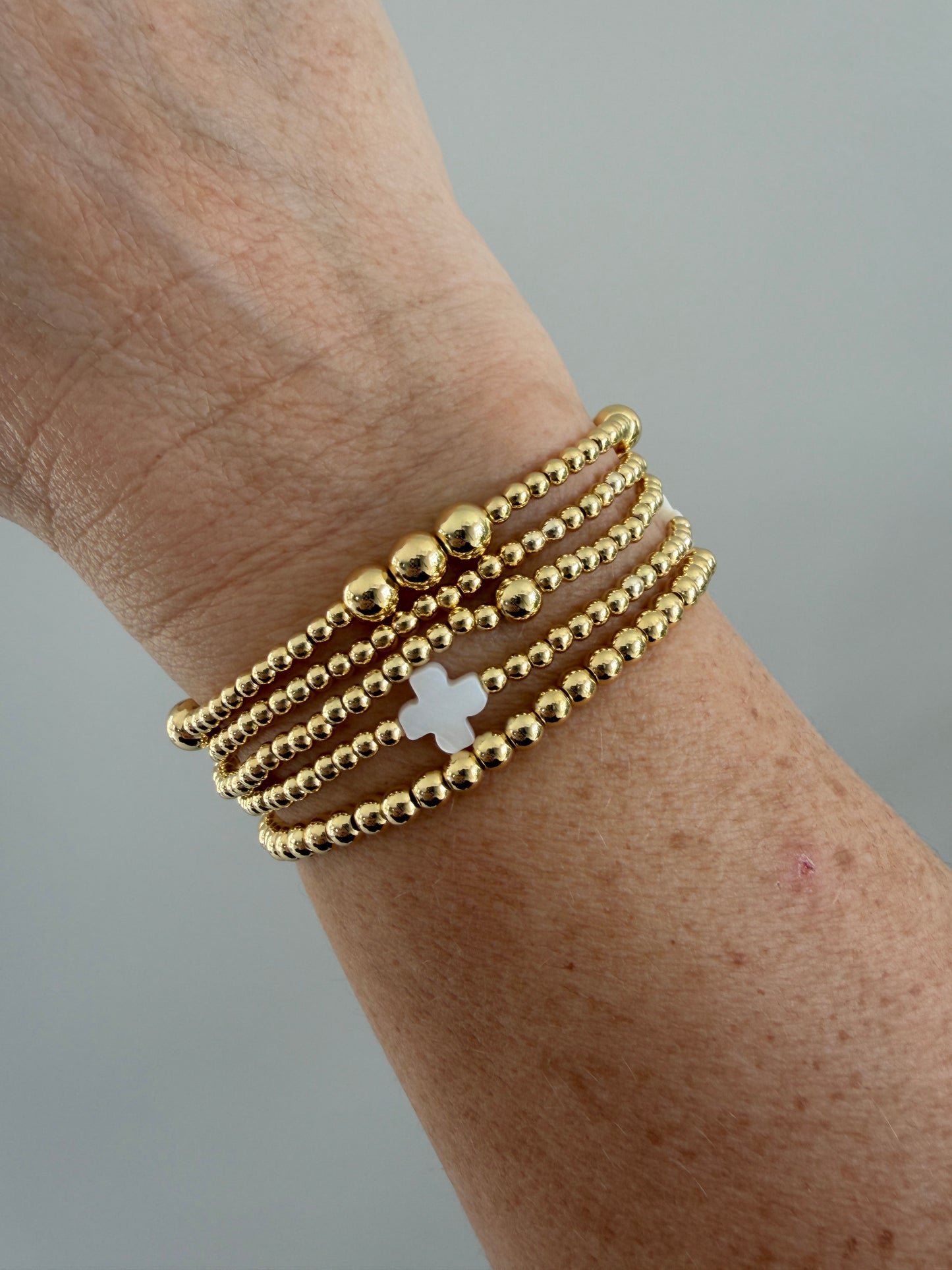 Stacked 18k gold-filled bracelets with white cross design, handmade beaded jewelry
