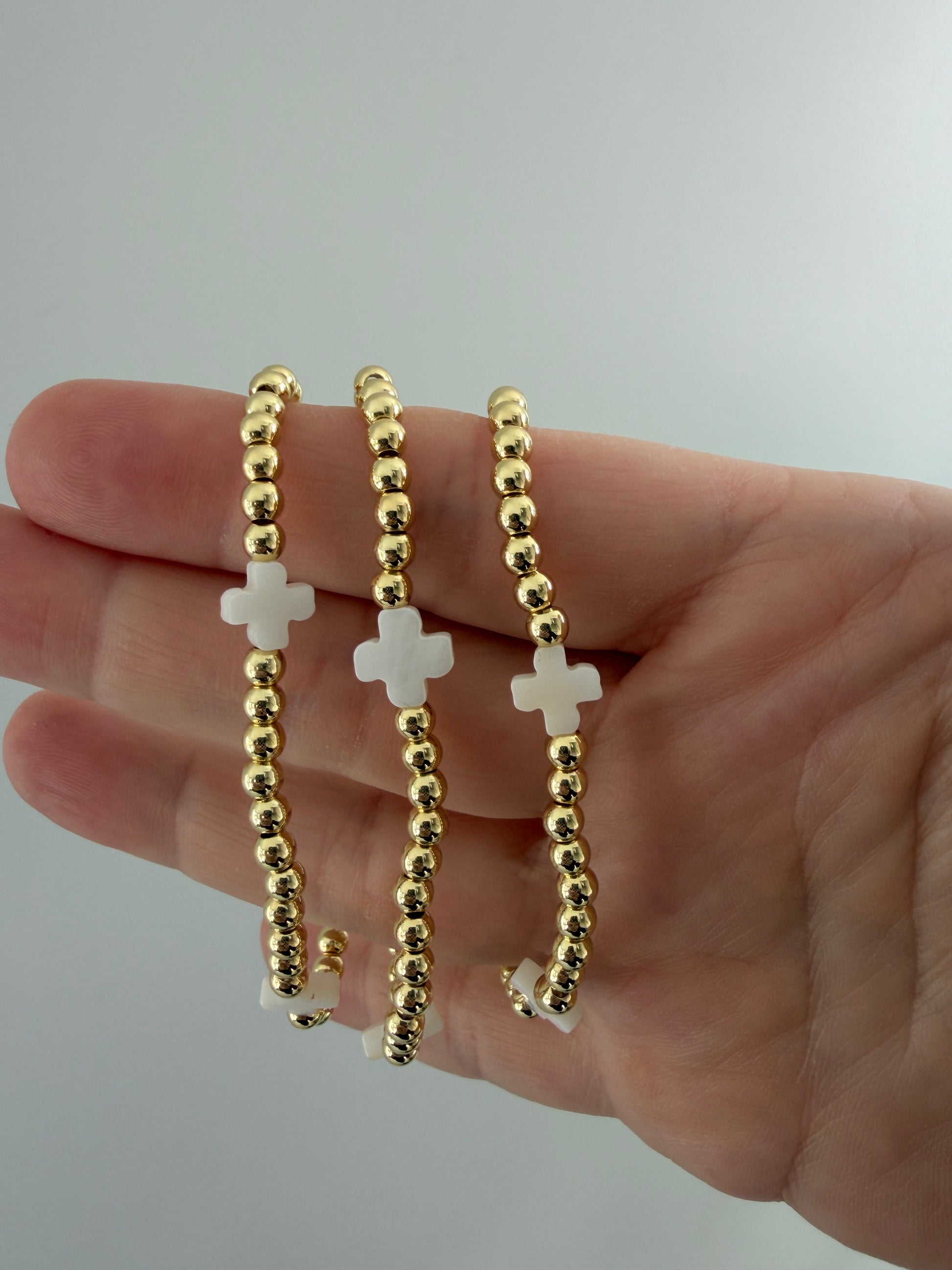 Gold beaded bracelet with white cross charms on a hand against a plain background