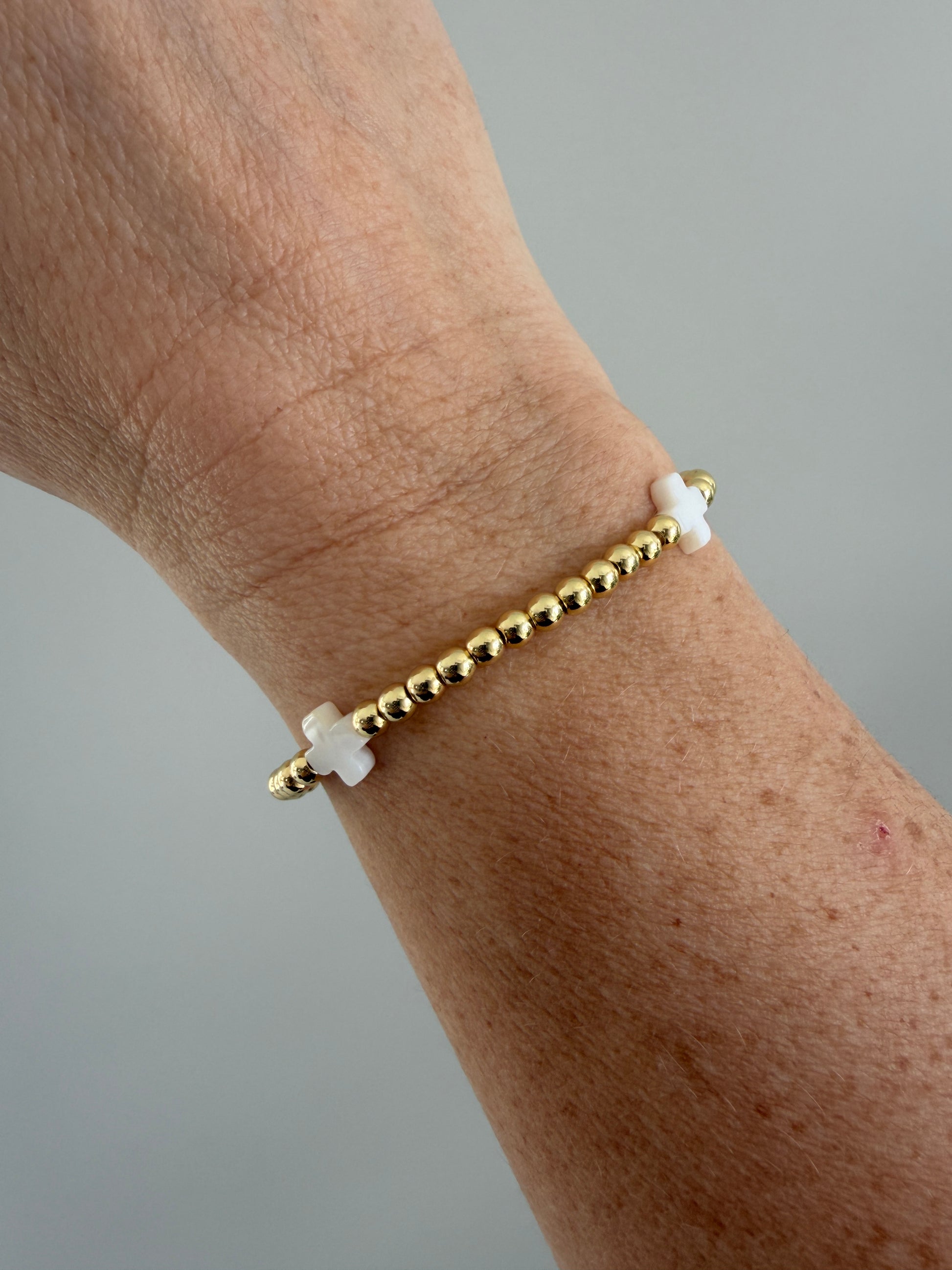 Gold beaded bracelet with white beads on a wrist against a gray background