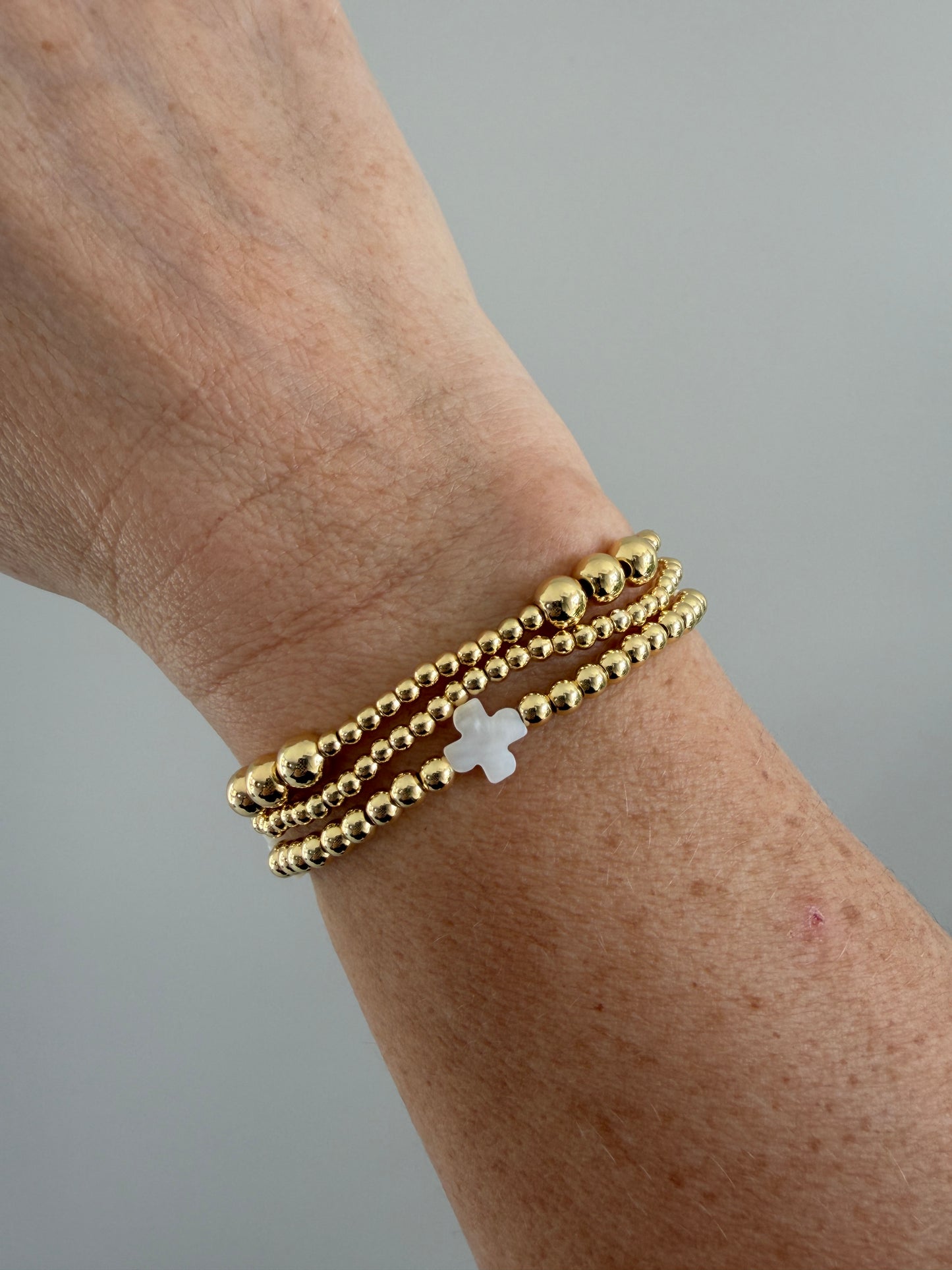Stacked 18k gold-filled bracelets with white cross design, handmade beaded jewelry