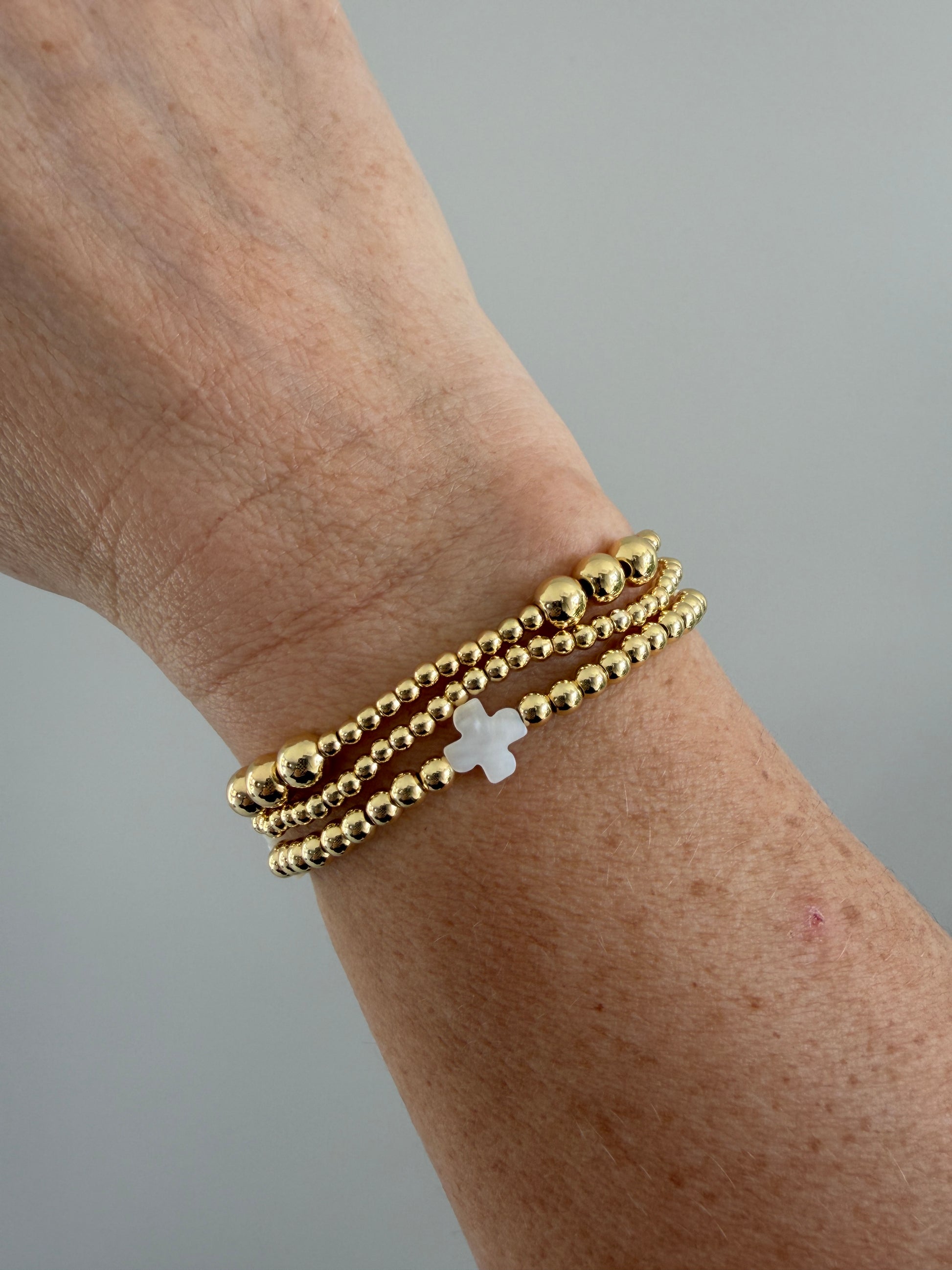 Stacked 18k gold-filled bracelets with white cross design, handmade beaded jewelry