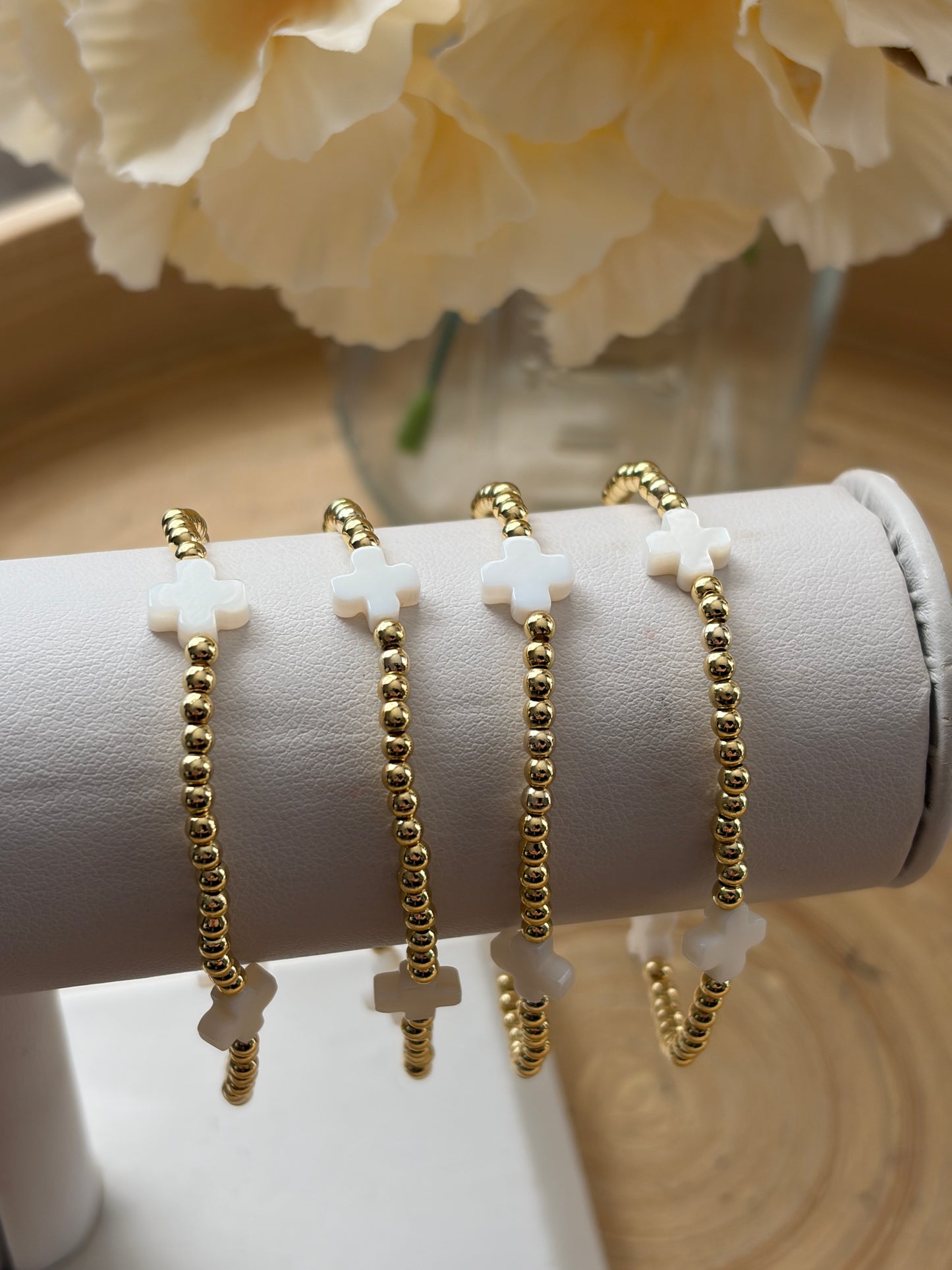 Gold bracelets on a white cylindrical stand with a blurred floral background